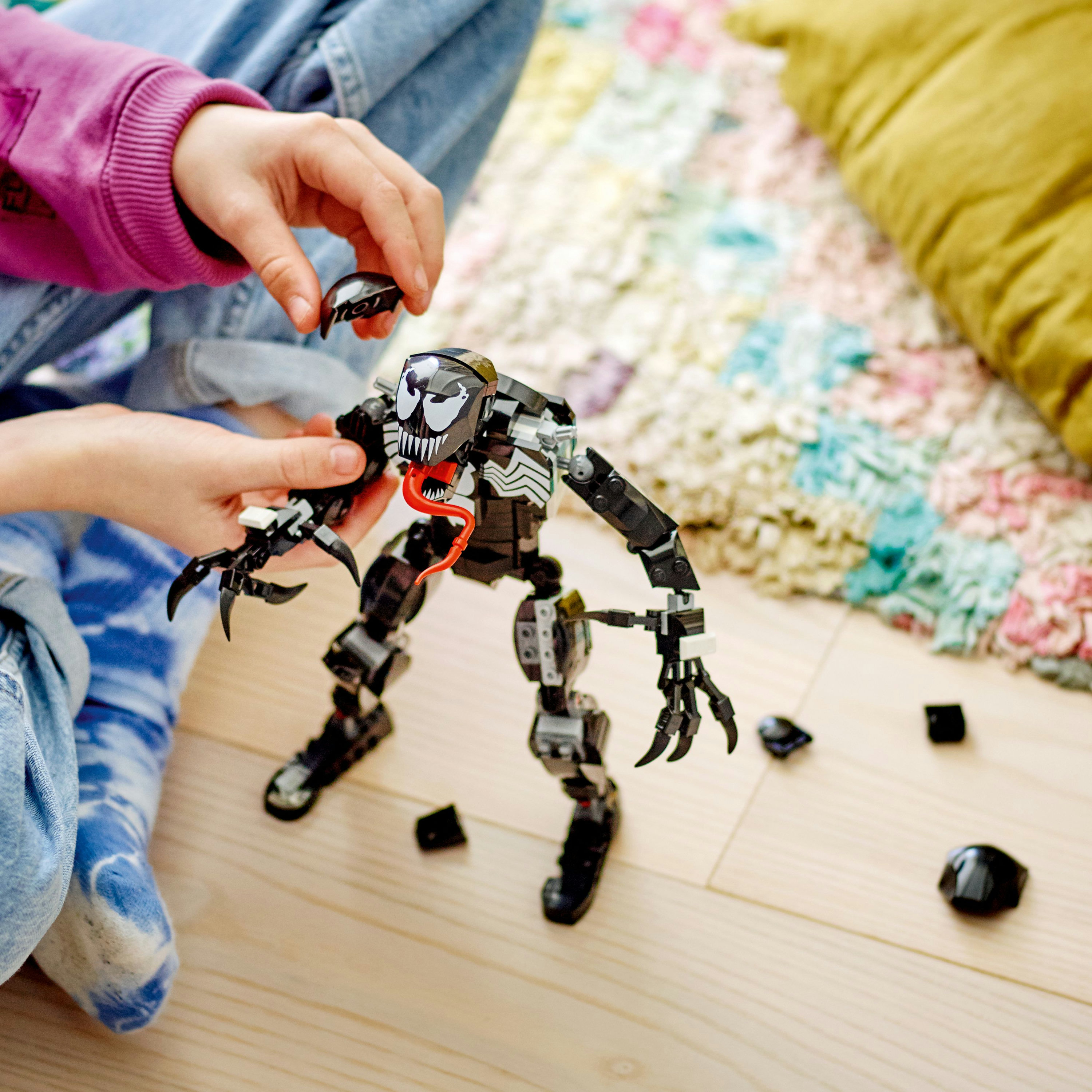Bir çocuk, siyah beyaz tasarımlı bir Lego Venom figürü topluyor.