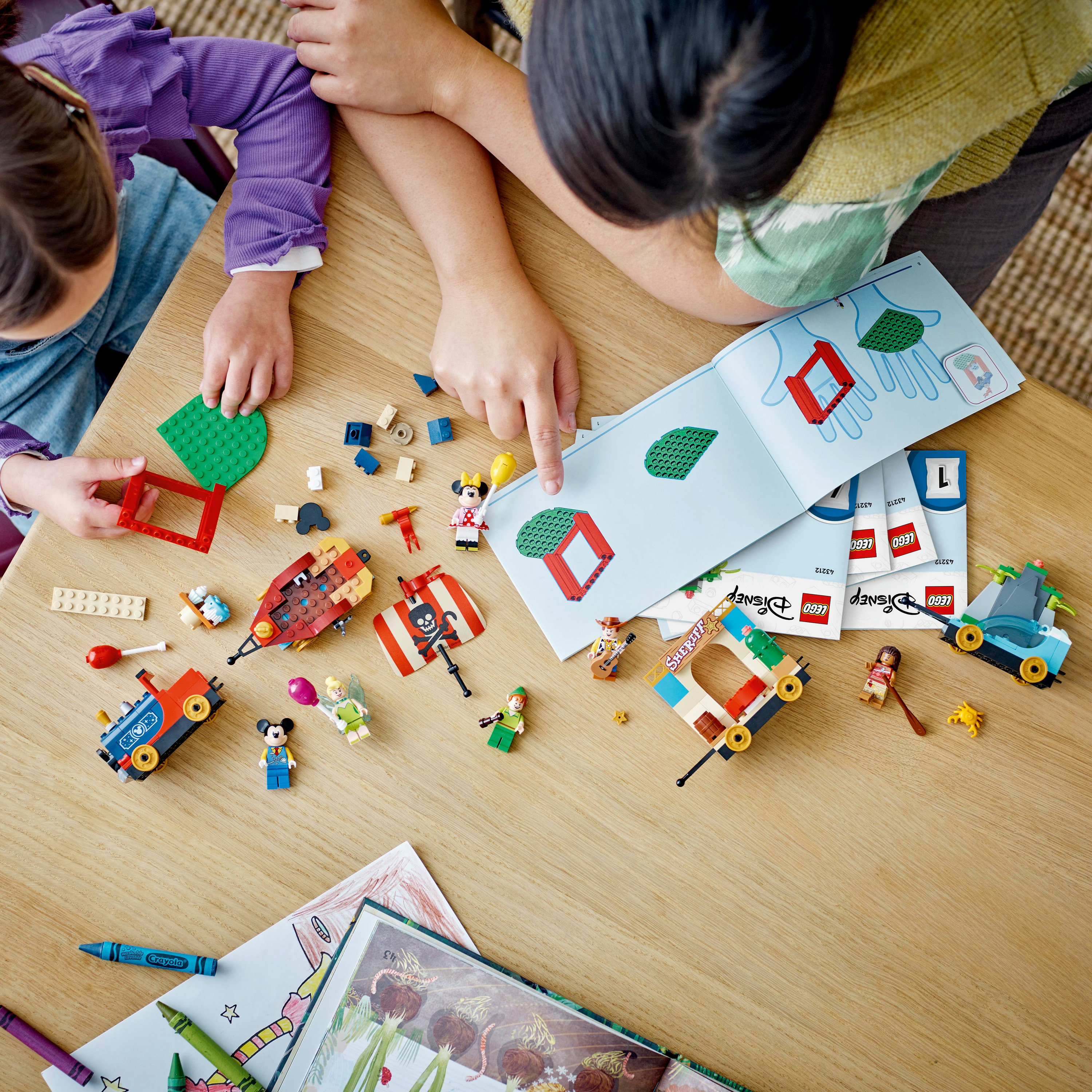Zestaw Lego w trakcie montażu. Dwie dziewczynki budują z różnych elementów. Instrukcje i rysunki są obecne.