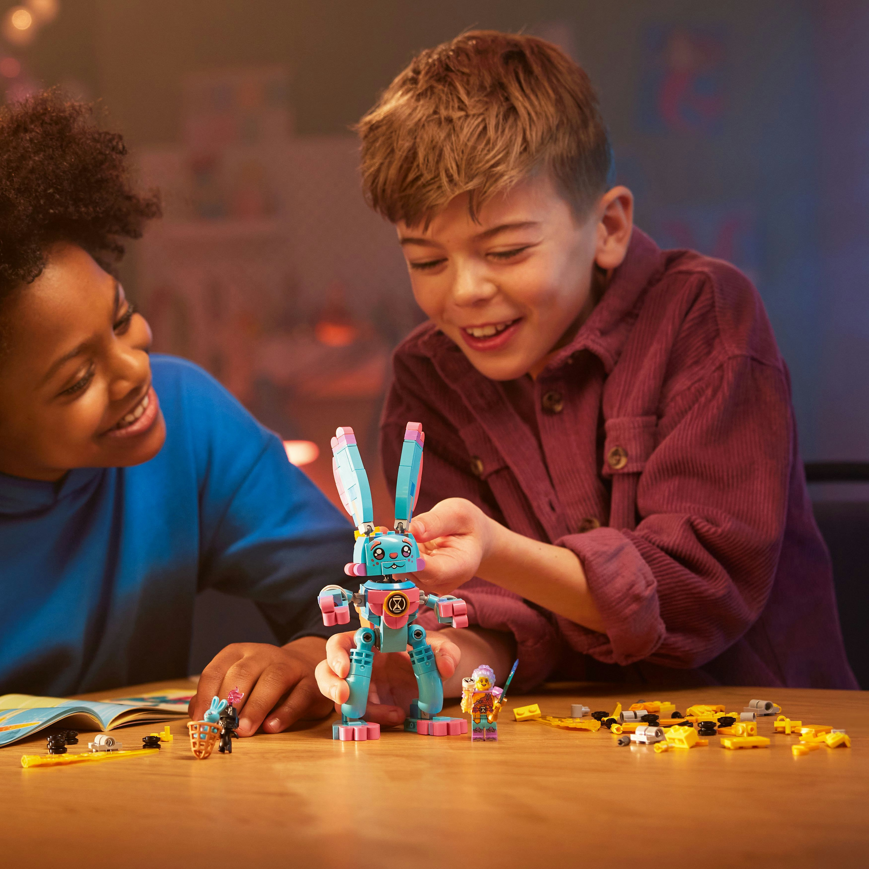 İki çocuk bir Lego robotu inşa ediyor. Önlerinde Lego parçaları olan bir masa var.