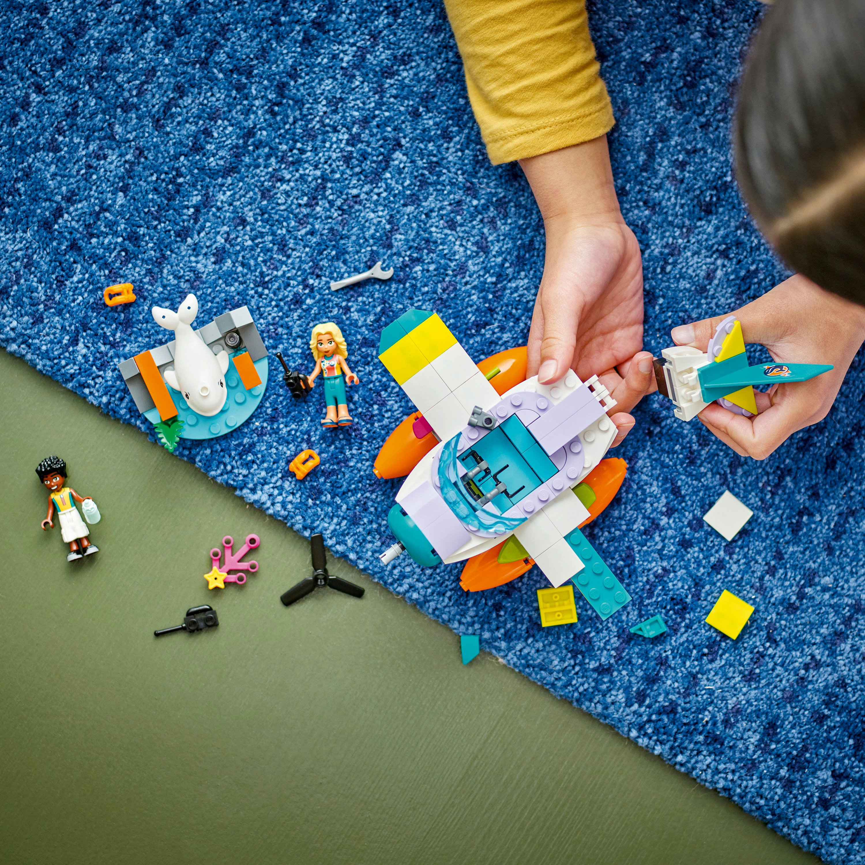 Un enfant joue avec des jouets LEGO Friends, construisant un bateau et des figurines sur un tapis bleu.