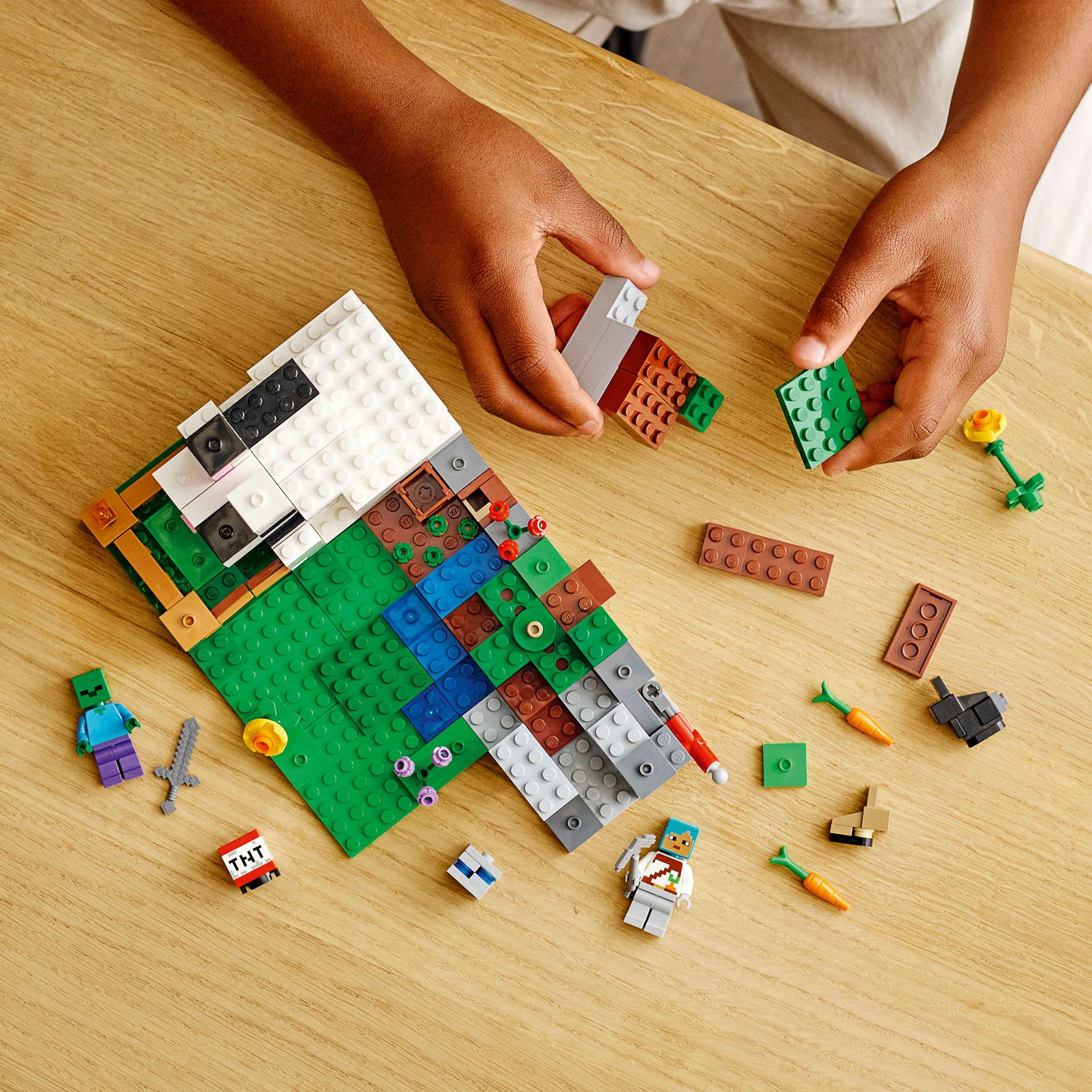 Mani che costruiscono Lego. I pezzi sono su un tavolo di legno. Il Lego è a tema Minecraft.