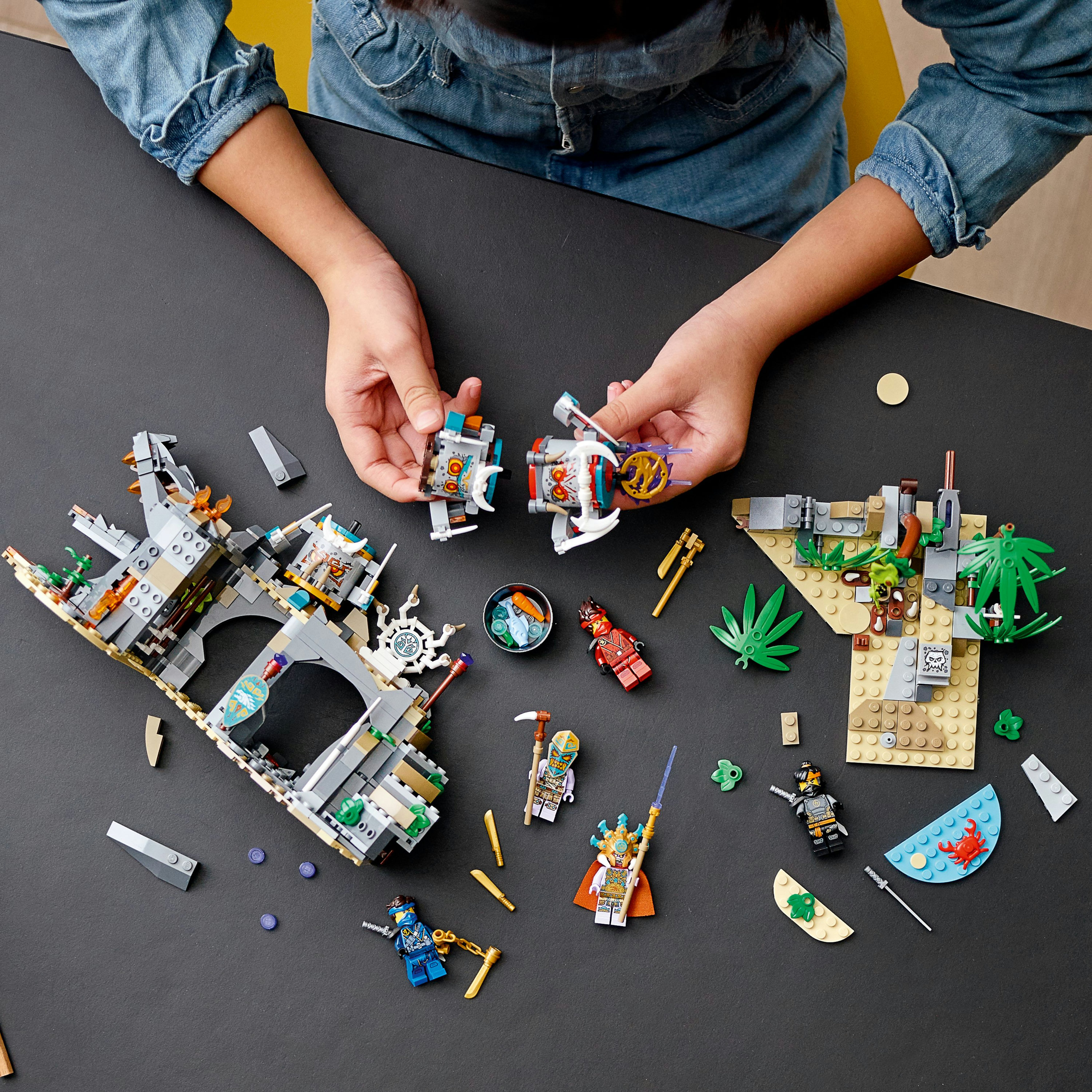 Lego-Set mit Figuren und Teilen. Kinderhände ordnen die Teile auf einem schwarzen Tisch an.
