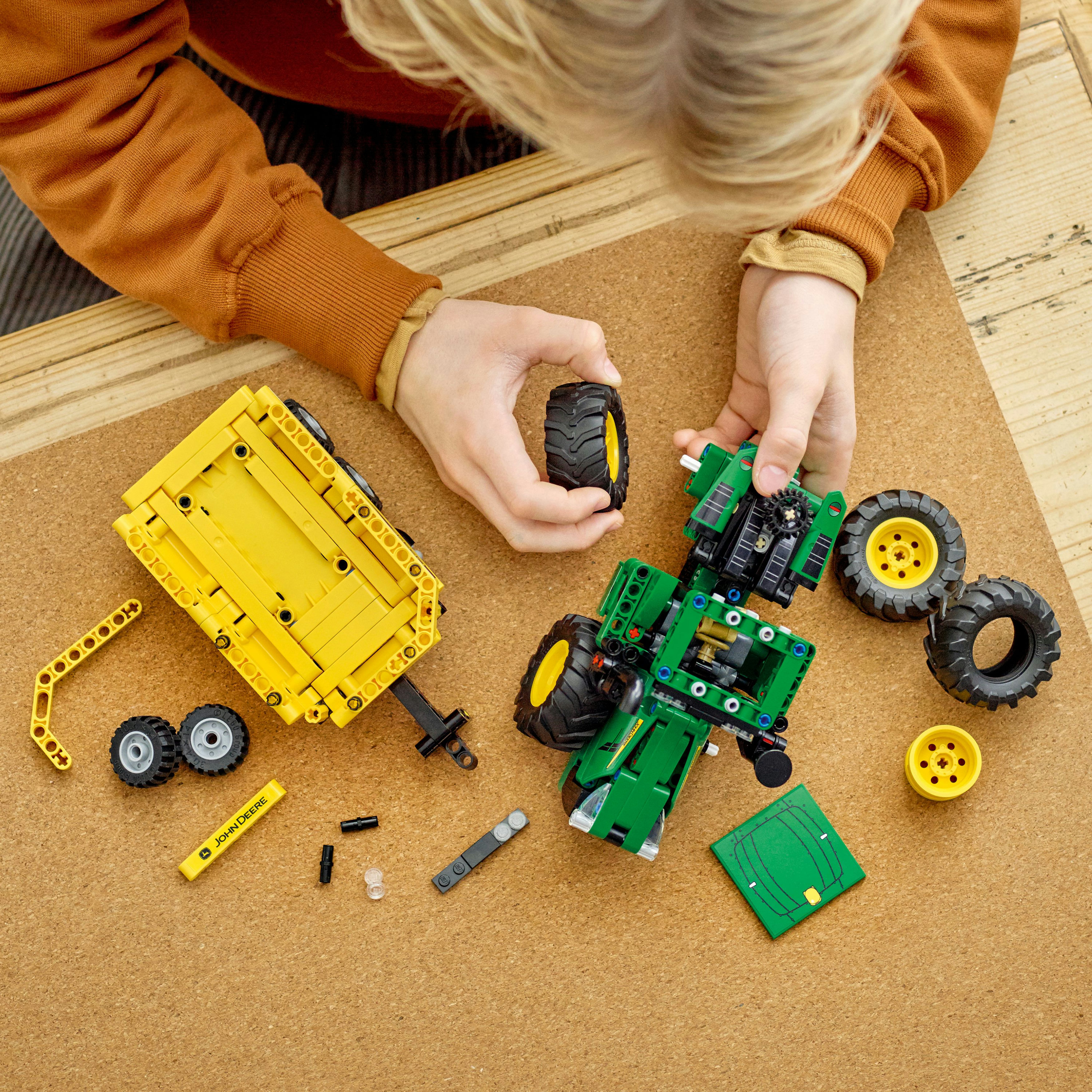 Bambino che assembla un trattore Lego John Deere, circondato da pezzi su una tavola di sughero.