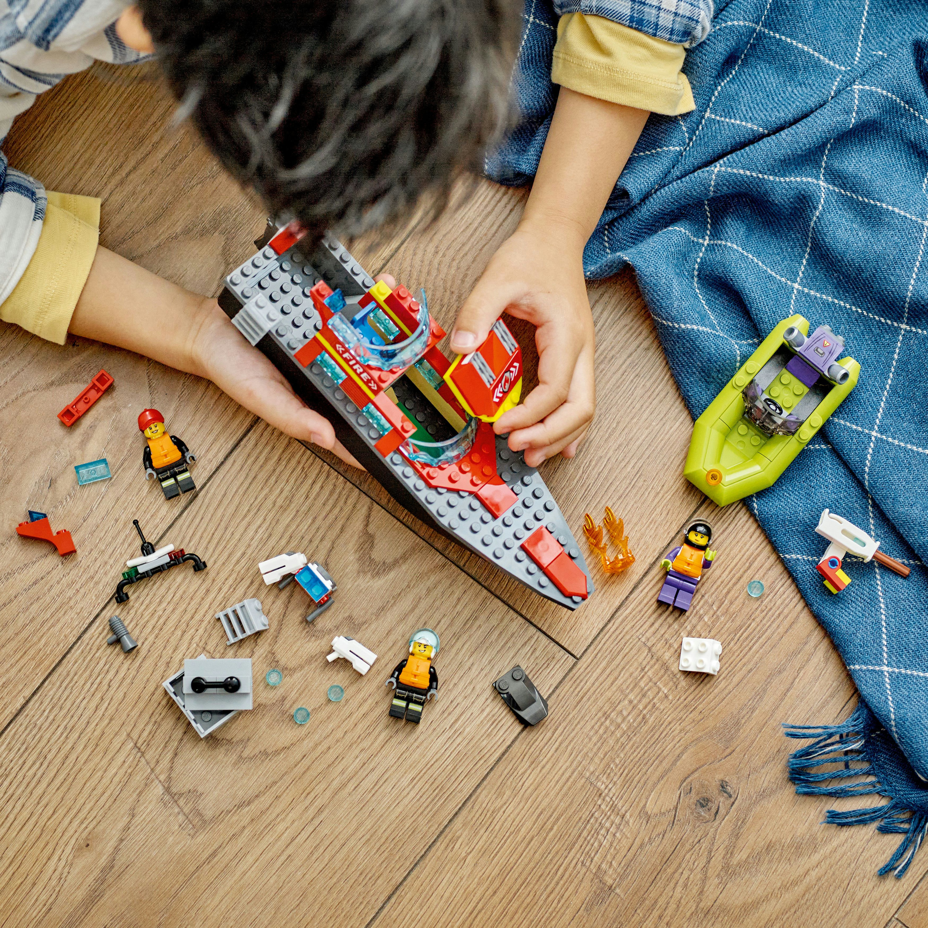 Un niño está ensamblando un barco Lego y varias piezas en un piso de madera.