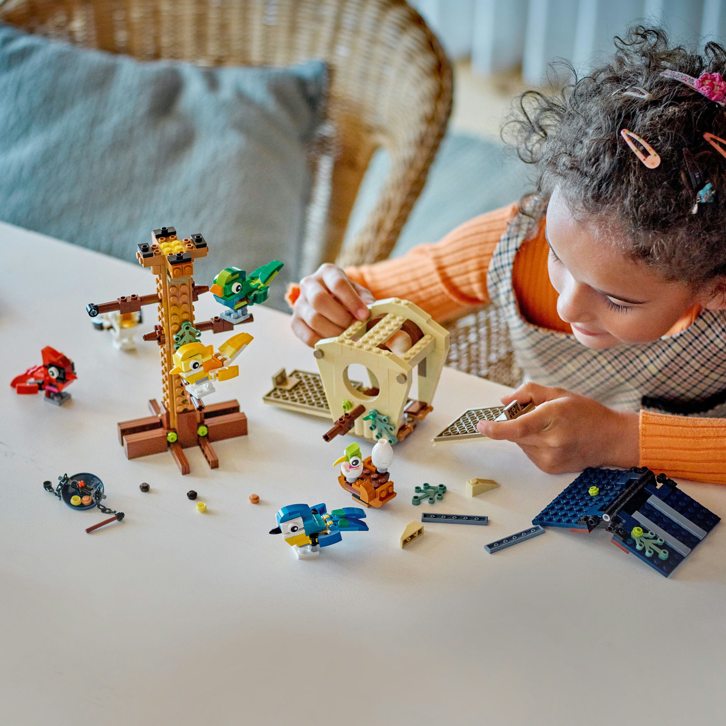 Dziewczynka buduje ptaki Lego na białym stole. Różne modele i części Lego są rozrzucone.