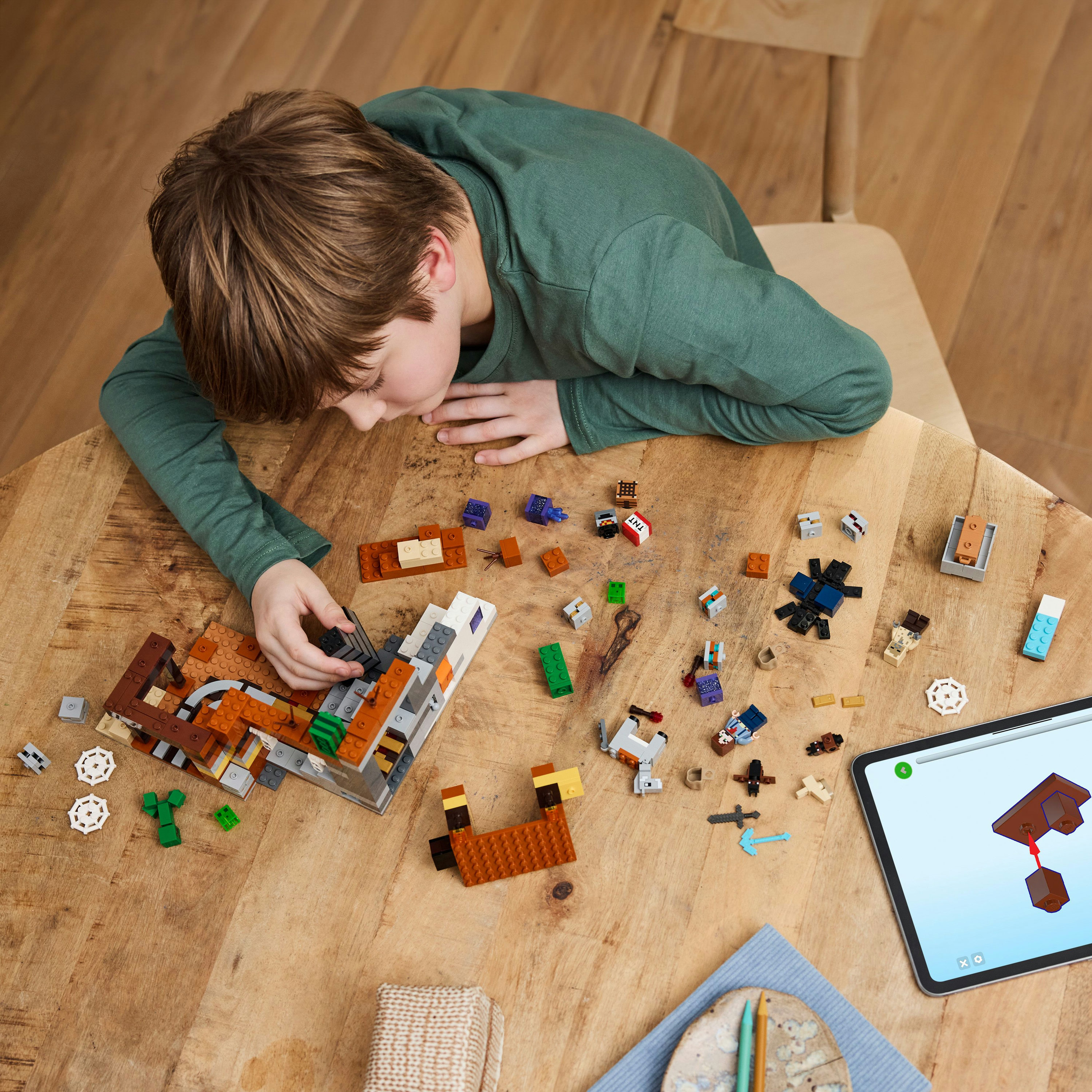 Jongen bouwt met LEGO-stenen op een houten tafel. Een tablet toont instructies.