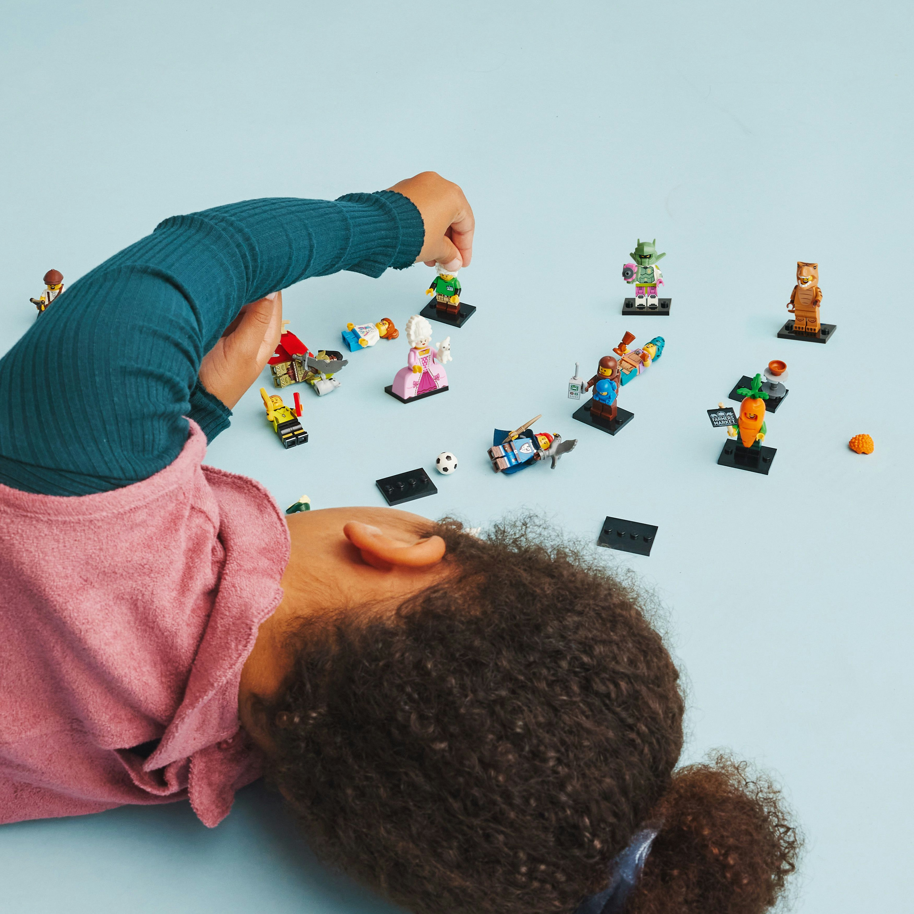 Ein Kind spielt mit Lego-Minifiguren, verteilt auf einer blauen Oberfläche.