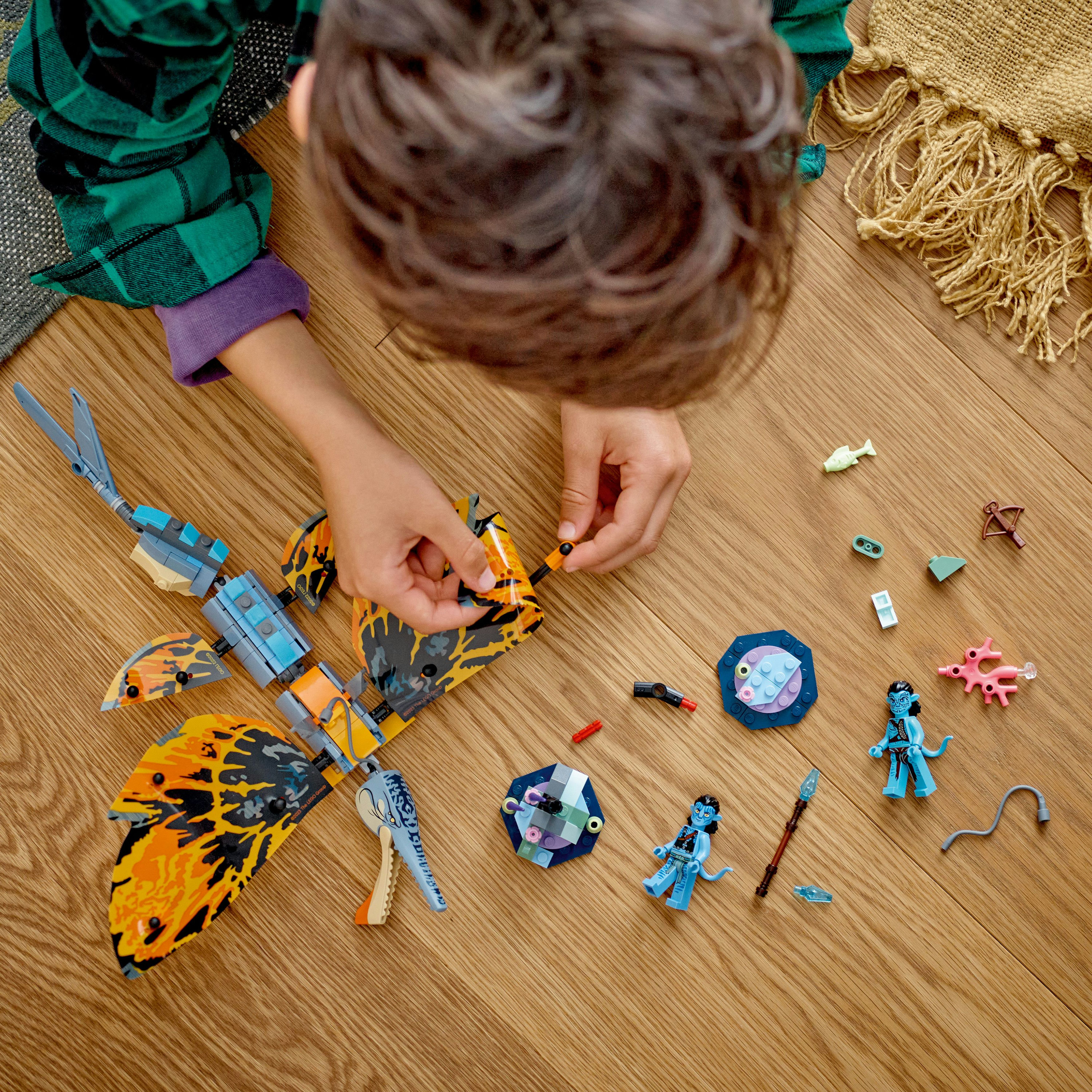 Un bambino che costruisce un set Lego Avatar. Ci sono personaggi e pezzi Lego sul legno.
