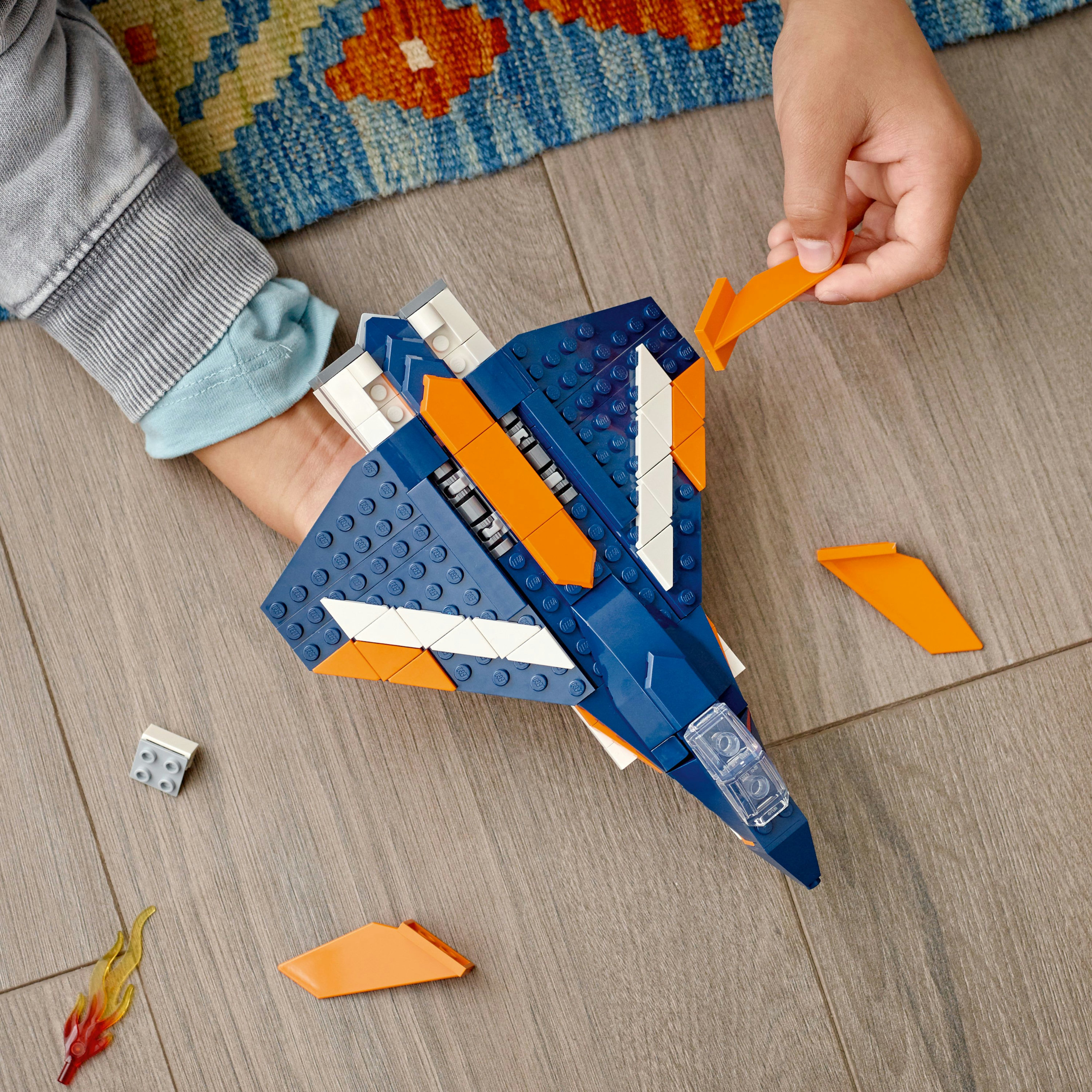 Las manos de un niño montan un avión Lego azul y naranja, con aletas naranjas en el lateral.
