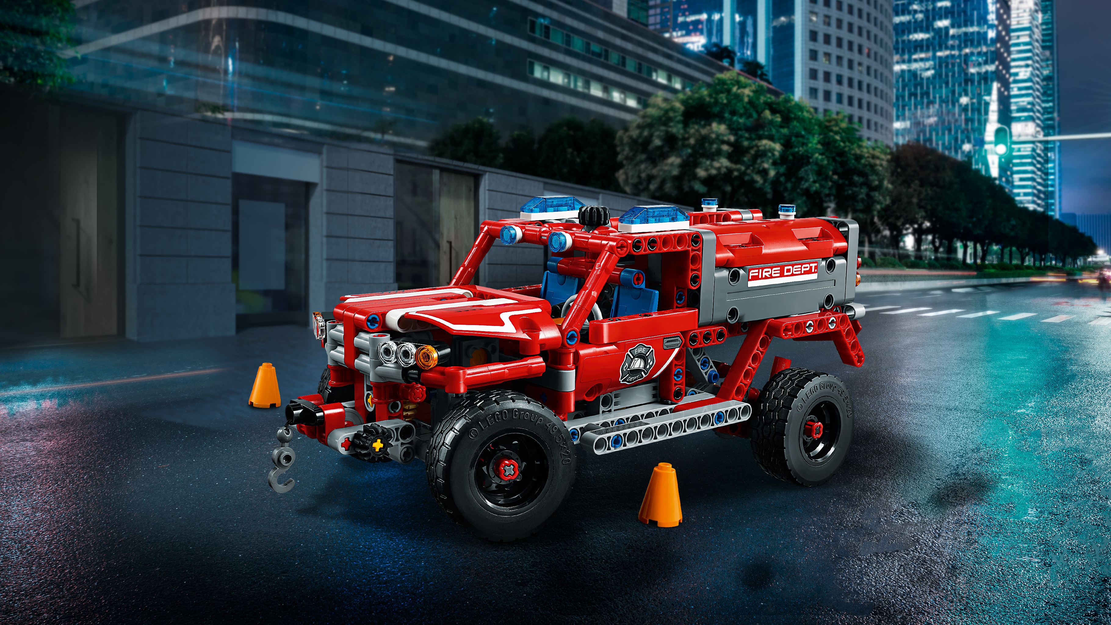 Zabawka LEGO Technic - wóz strażacki. Czerwona ciężarówka z niebieskimi światłami, hakiem i pomarańczowymi pachołkami.