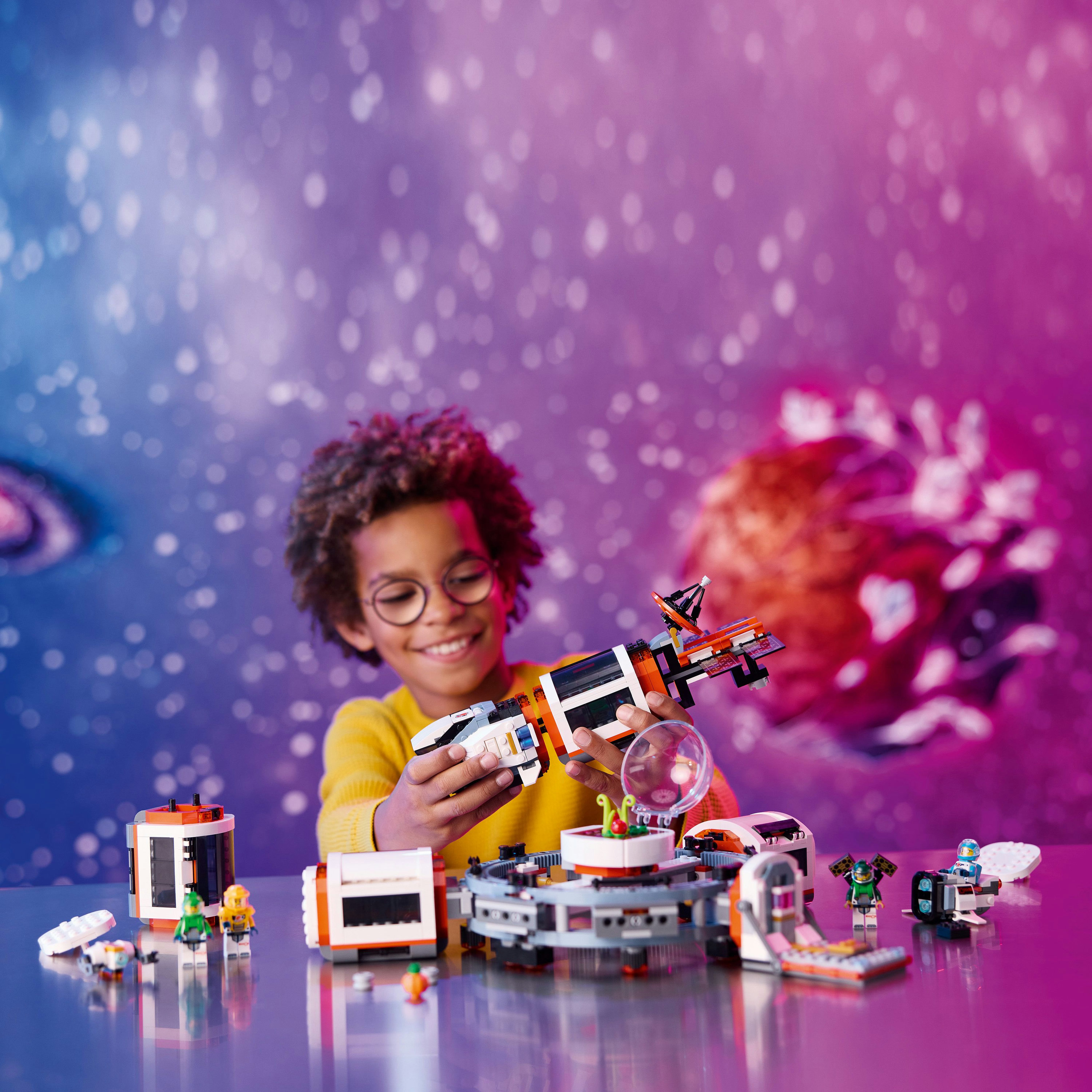 Niño jugando con set de Lego. Tema espacial, con nave y otros elementos. Fondo morado y azul.