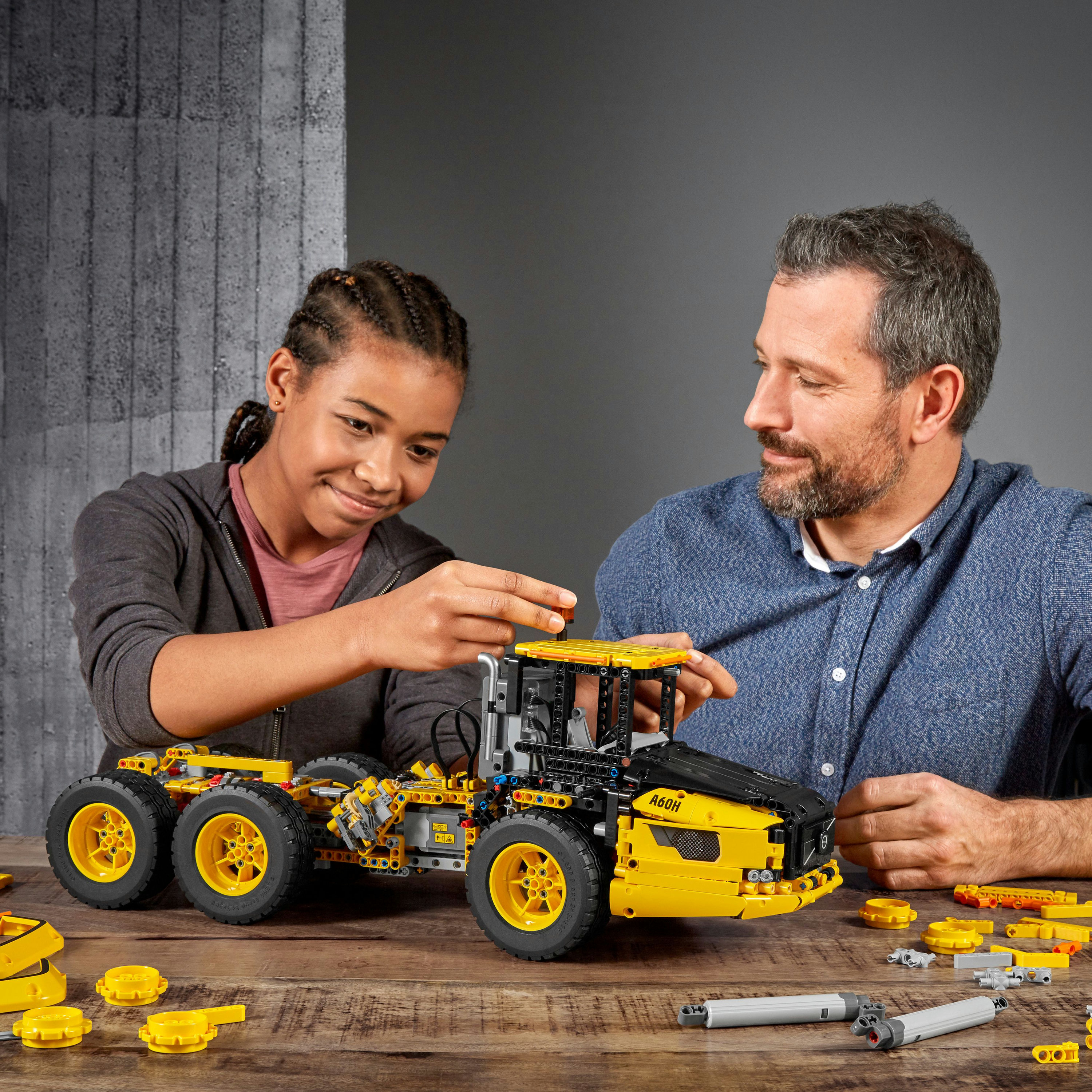 Due persone che costruiscono un camion Lego giallo. Strumenti e parti sparsi.