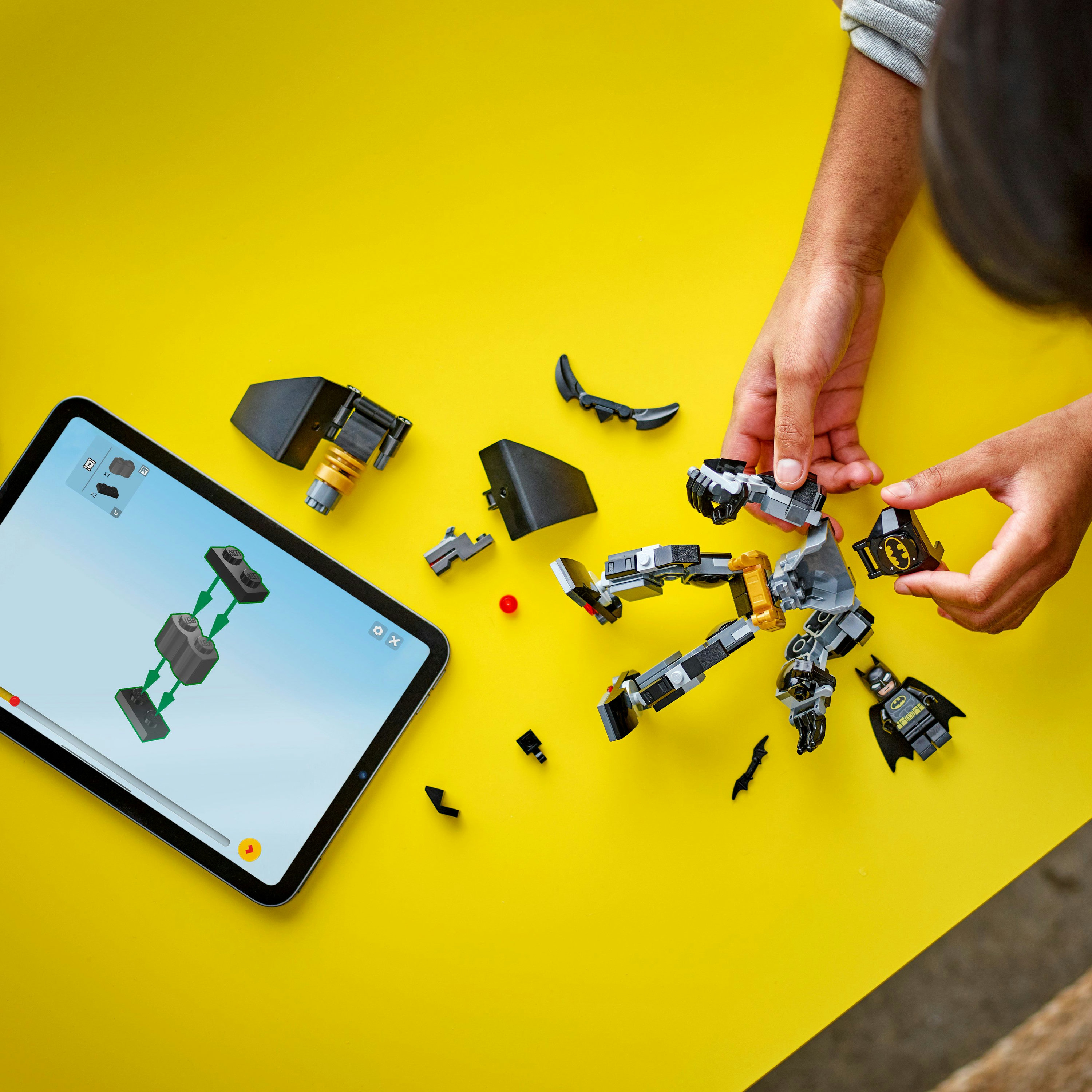 Ręce składające zestaw Lego Batmana. Tablet z instrukcjami leży obok elementów.