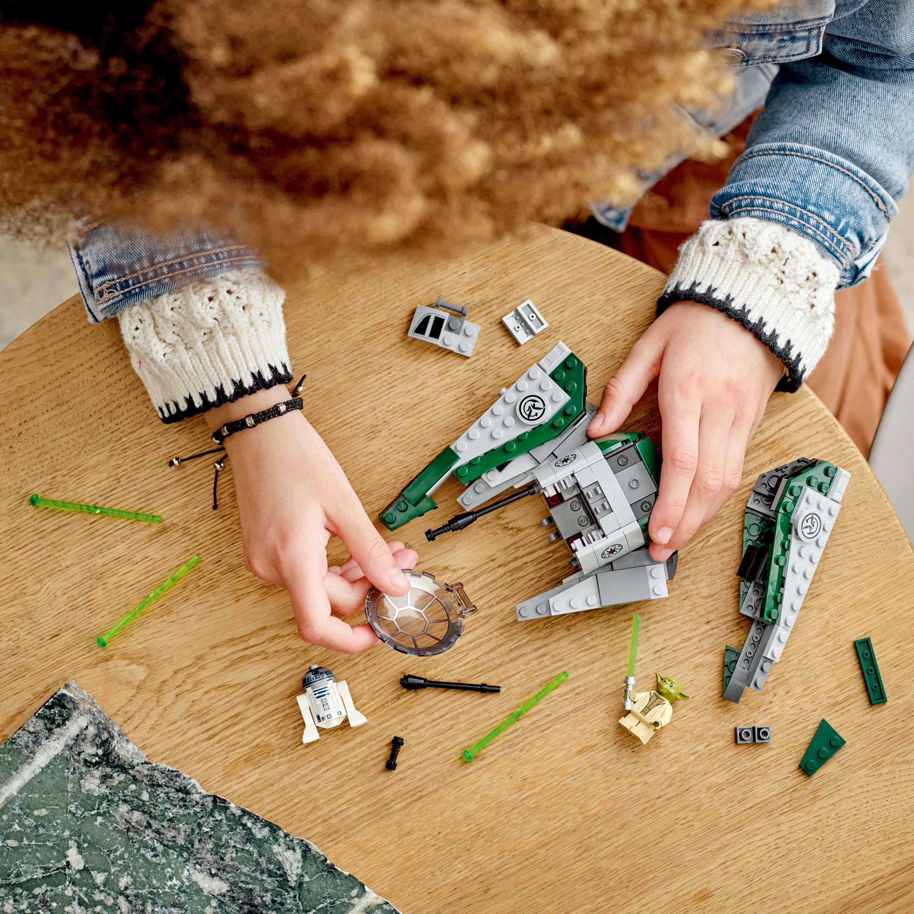 Hände einer Person, die Lego Star Wars Raumschiffmodelle auf einer Holzoberfläche zusammenbaut.