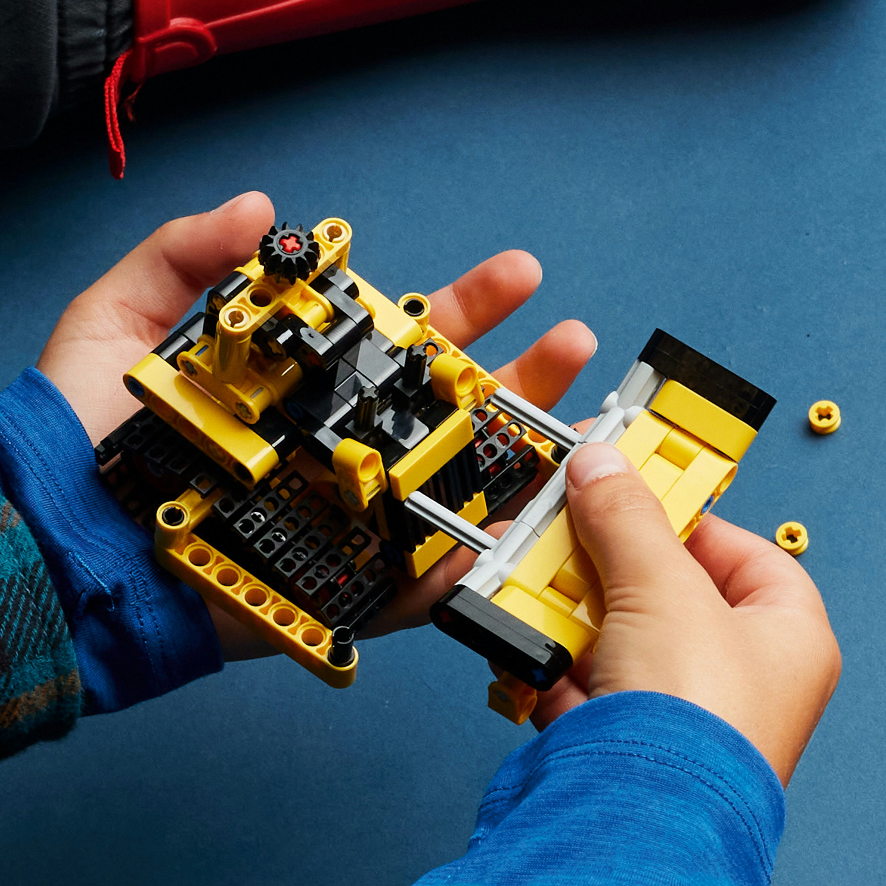 Mani che assemblano un set Lego bulldozer giallo e nero su una superficie blu.