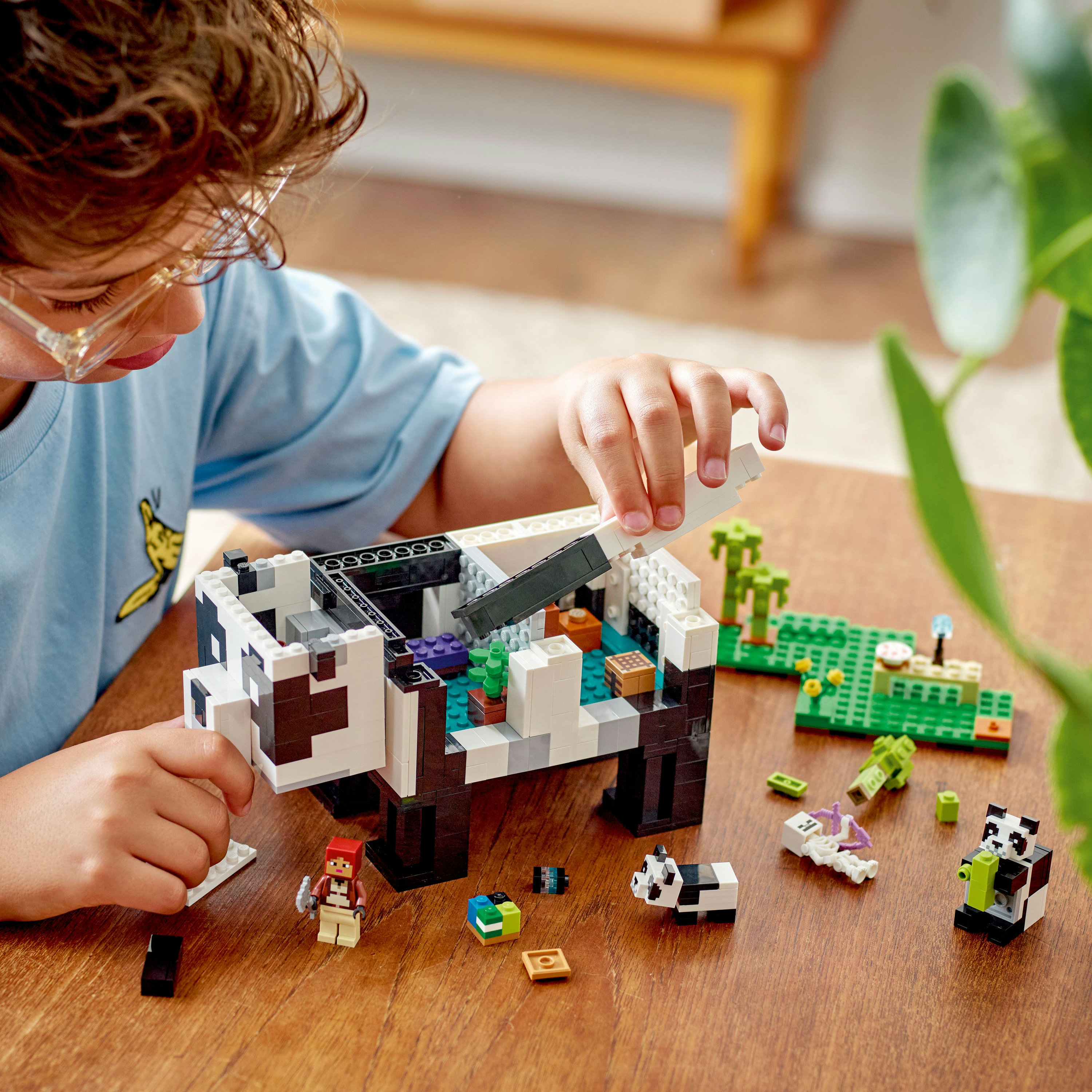 Bir çocuk bir panda Lego seti yapıyor. Masada çeşitli Lego parçaları var. Yeşil arka plan.