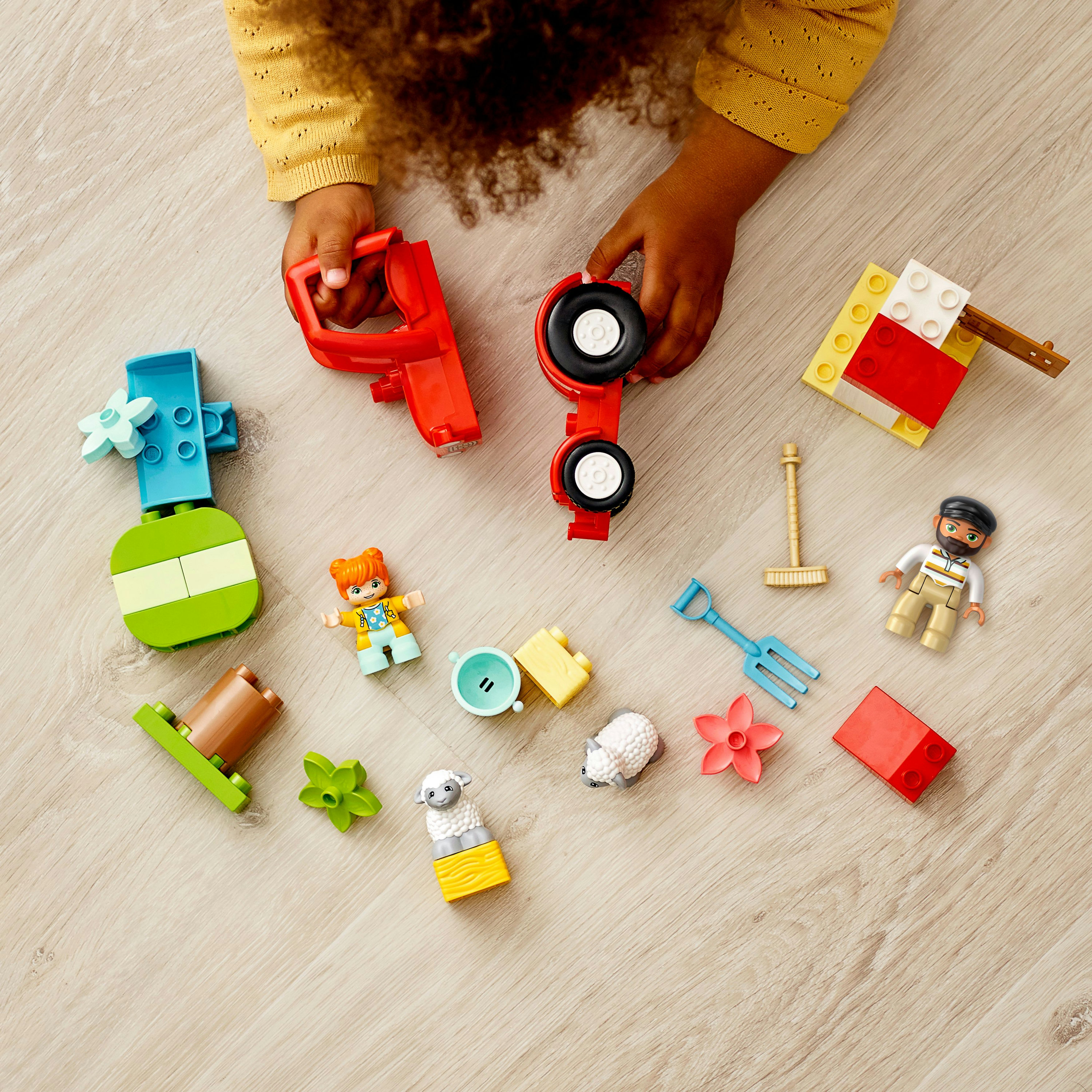 Ein Kind ist von Duplo-Lego-Steinen umgeben. Ein roter Traktor ist im Hintergrund.