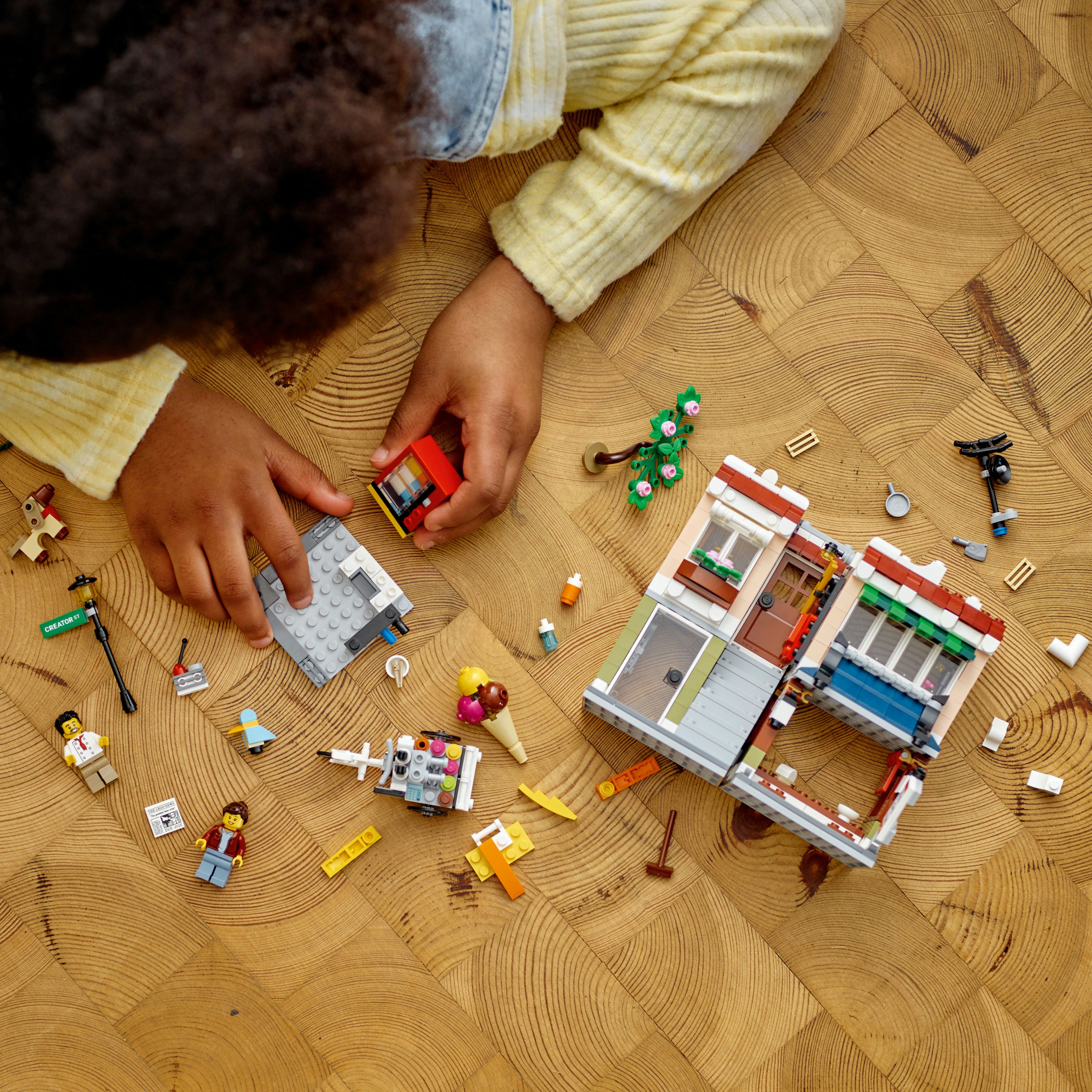Ein Kind spielt mit Lego-Steinen. Es gibt Gebäude, eine Straße und Mini-Figuren aus Lego.