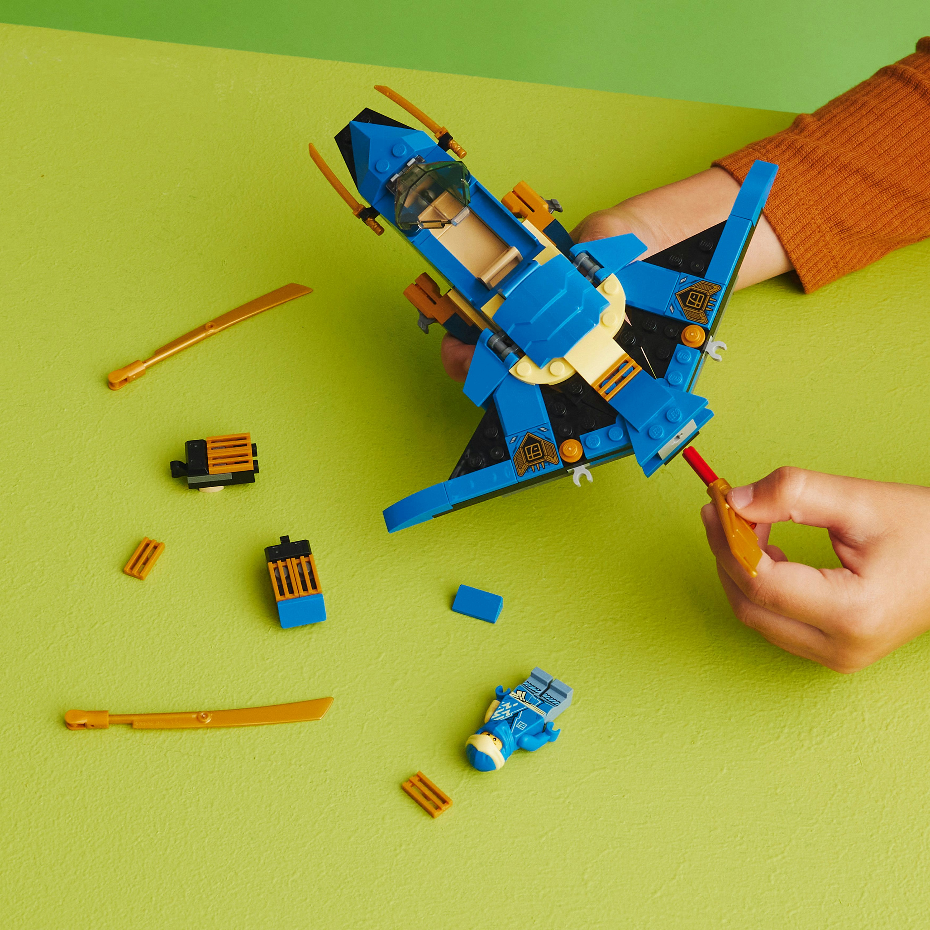 Ein blaues und schwarzes Lego Ninjago-Spielzeug wird mit Händen zusammengebaut. Grüner Hintergrund.