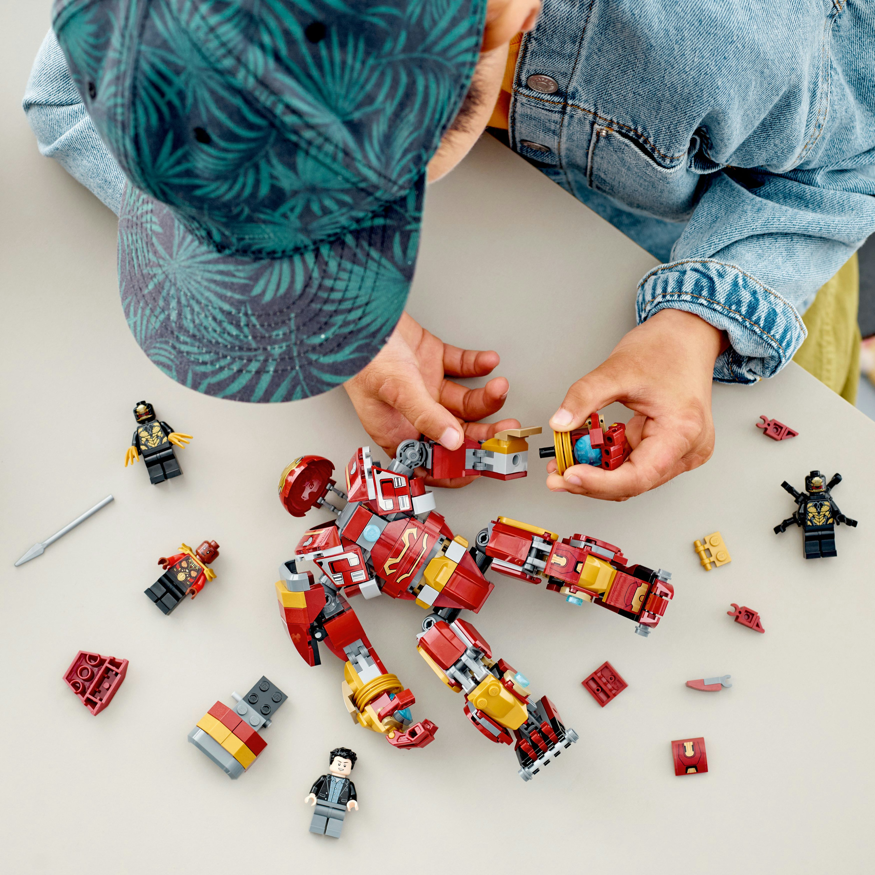 Hände, die Lego Iron Man Figur zusammensetzen, mit anderen Figuren und Teilen, auf einem Tisch.