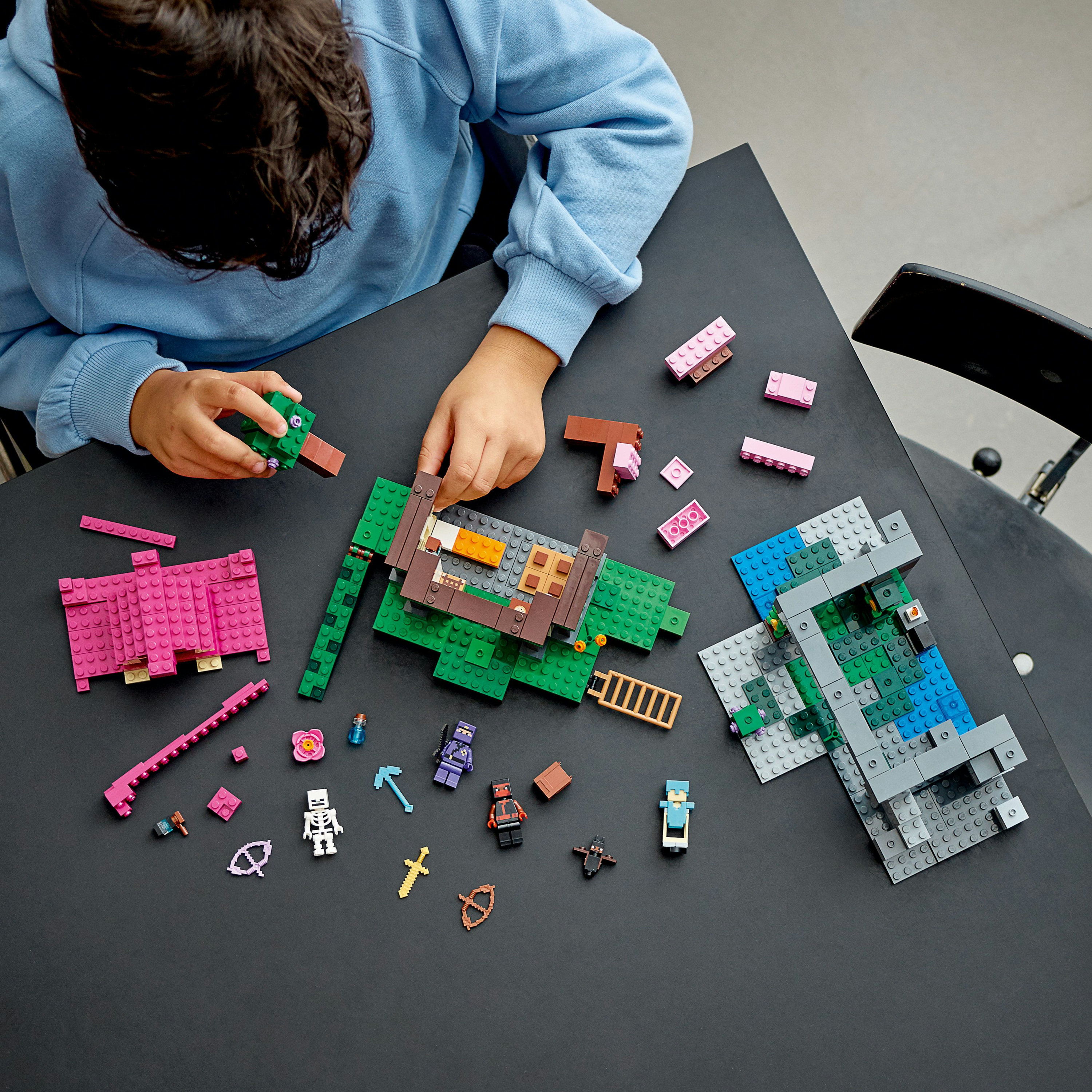 Kind spielt mit einem Lego-Set mit verschiedenen Figuren und Teilen auf einem schwarzen Tisch.
