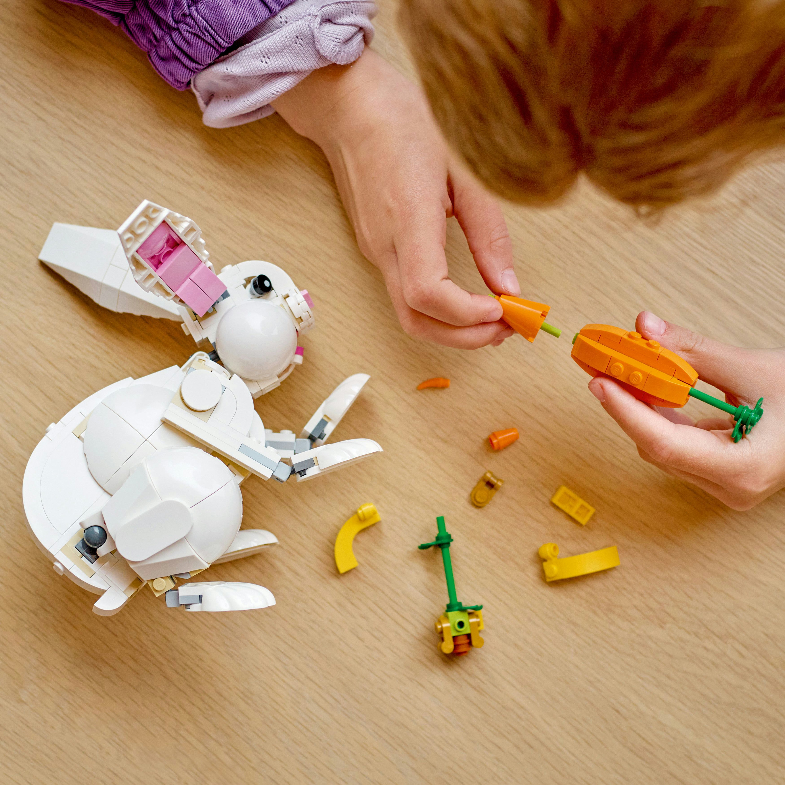 Hände eines Kindes, das einen weißen Lego-Hasen mit Karotte zusammensetzt.