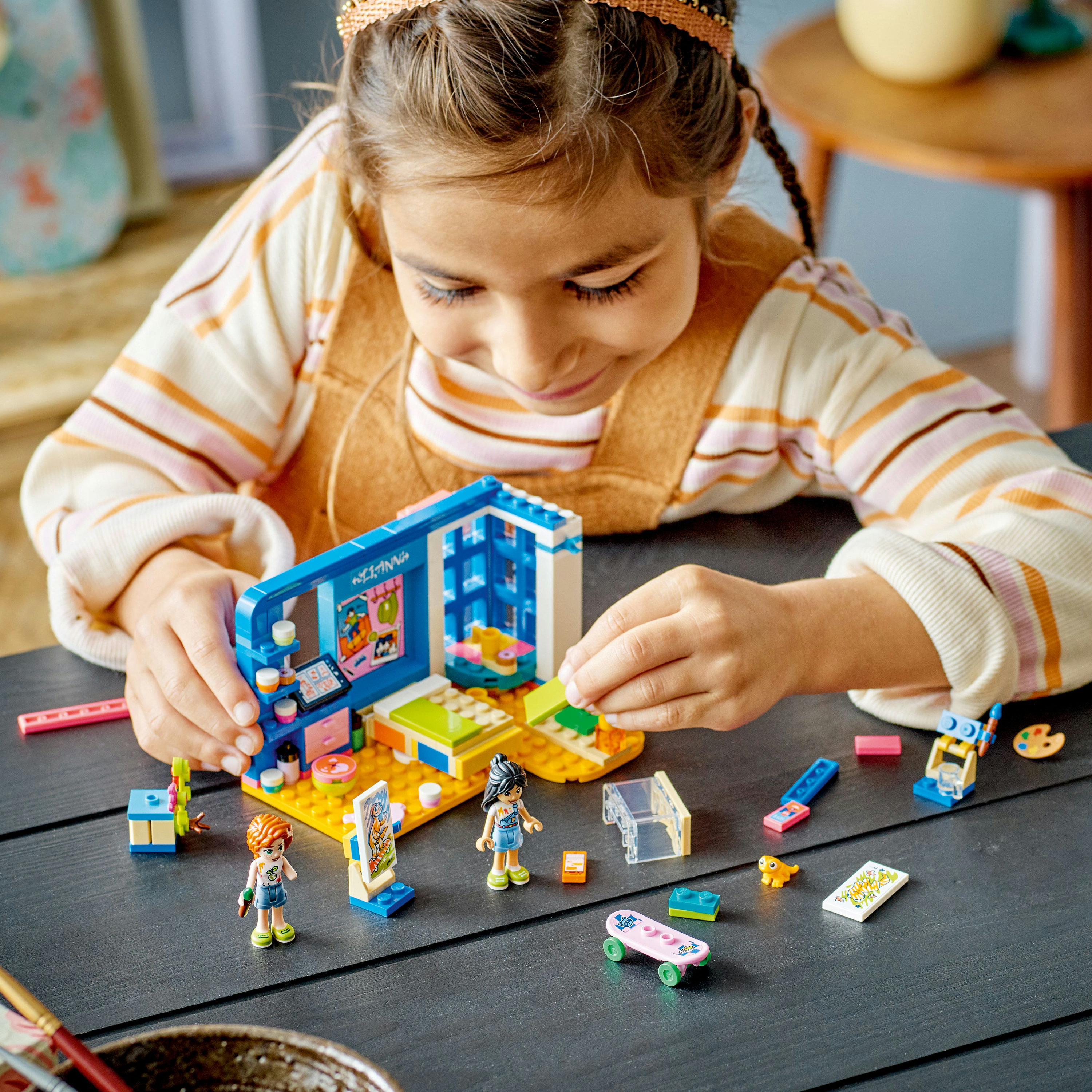 A girl playing with a Lego Friends set, building a studio with miniature art supplies and figures.