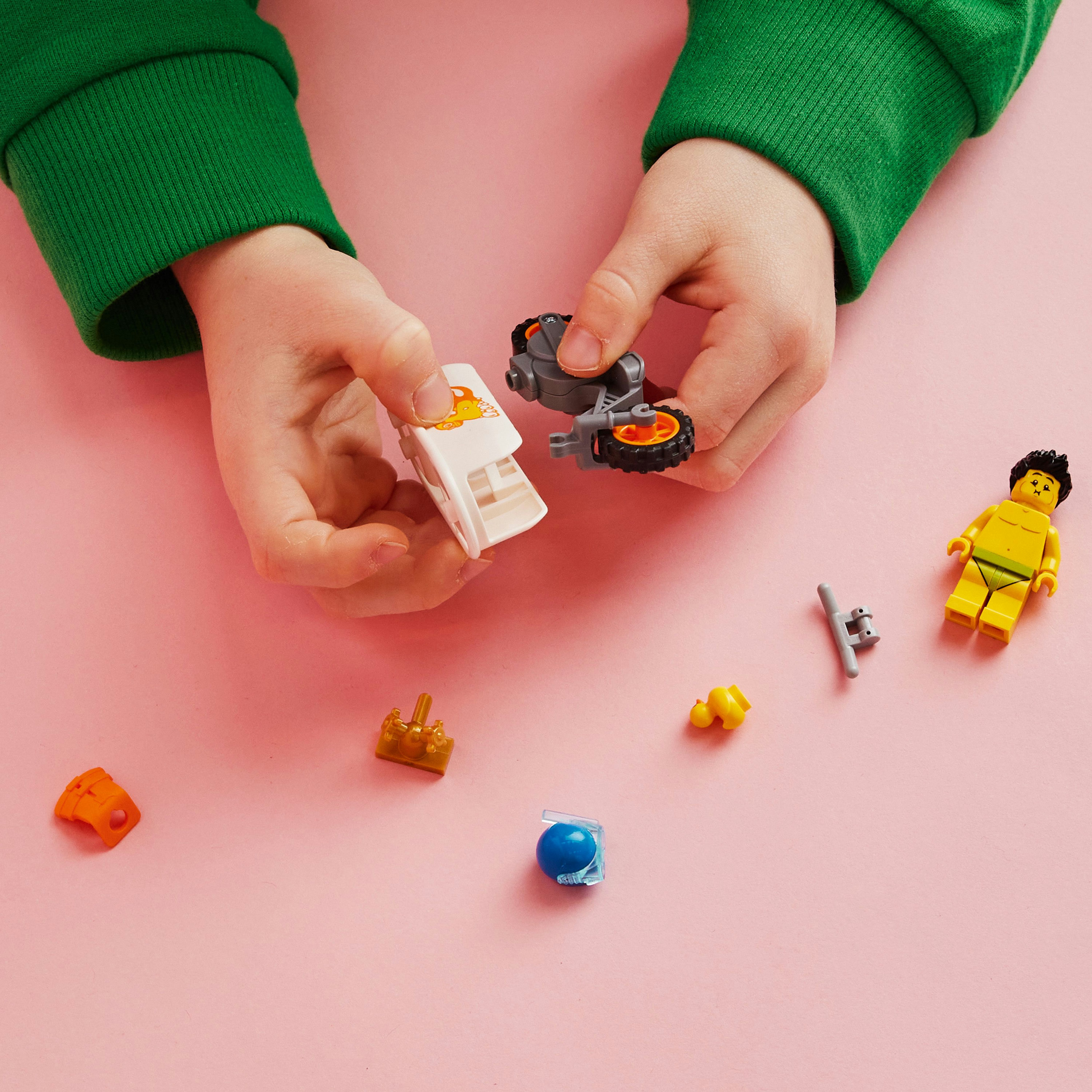 Ręce dziecka składające klocki LEGO na różowej powierzchni.