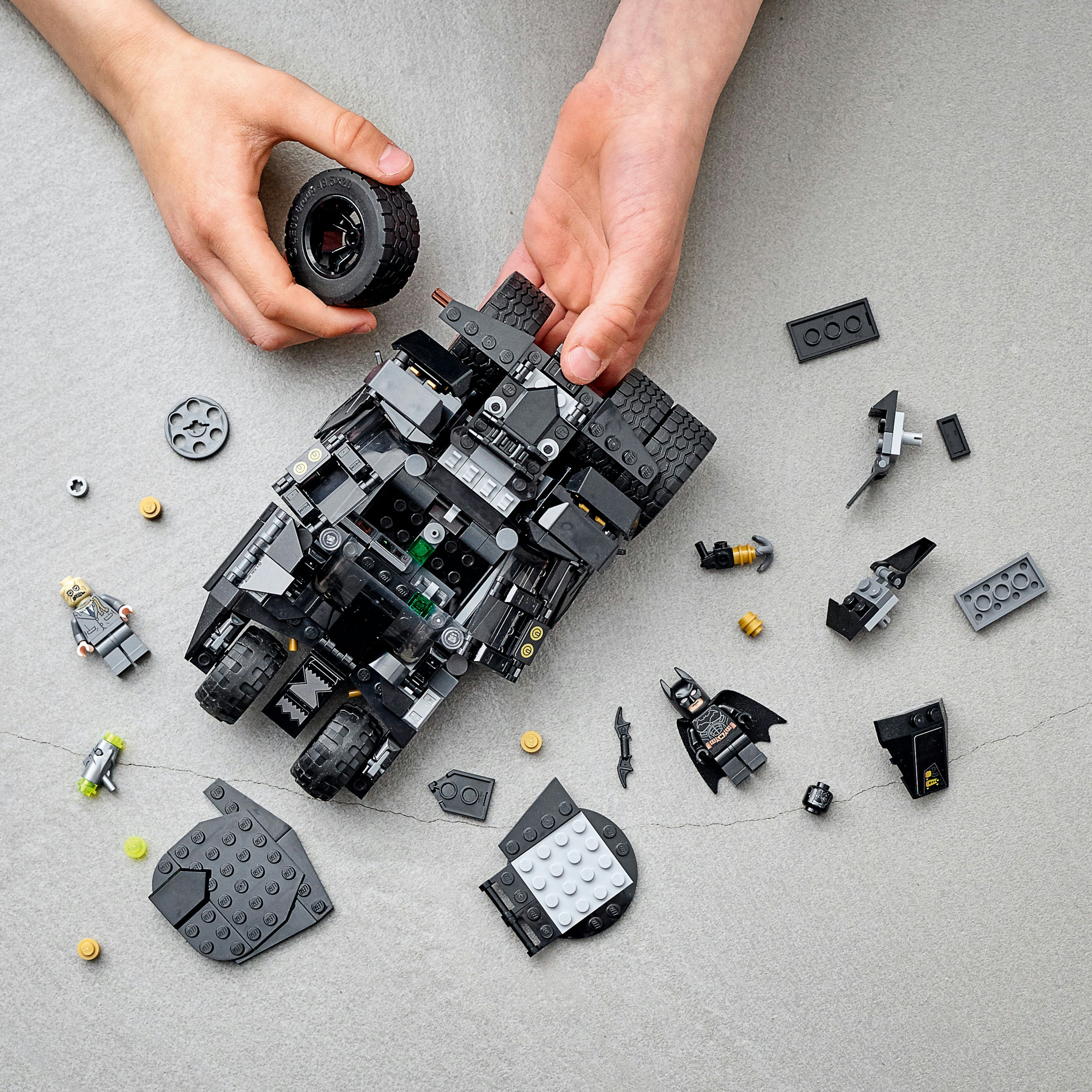 Handen houden een band vast, zwarte Lego Batmobile en losse Lego.
