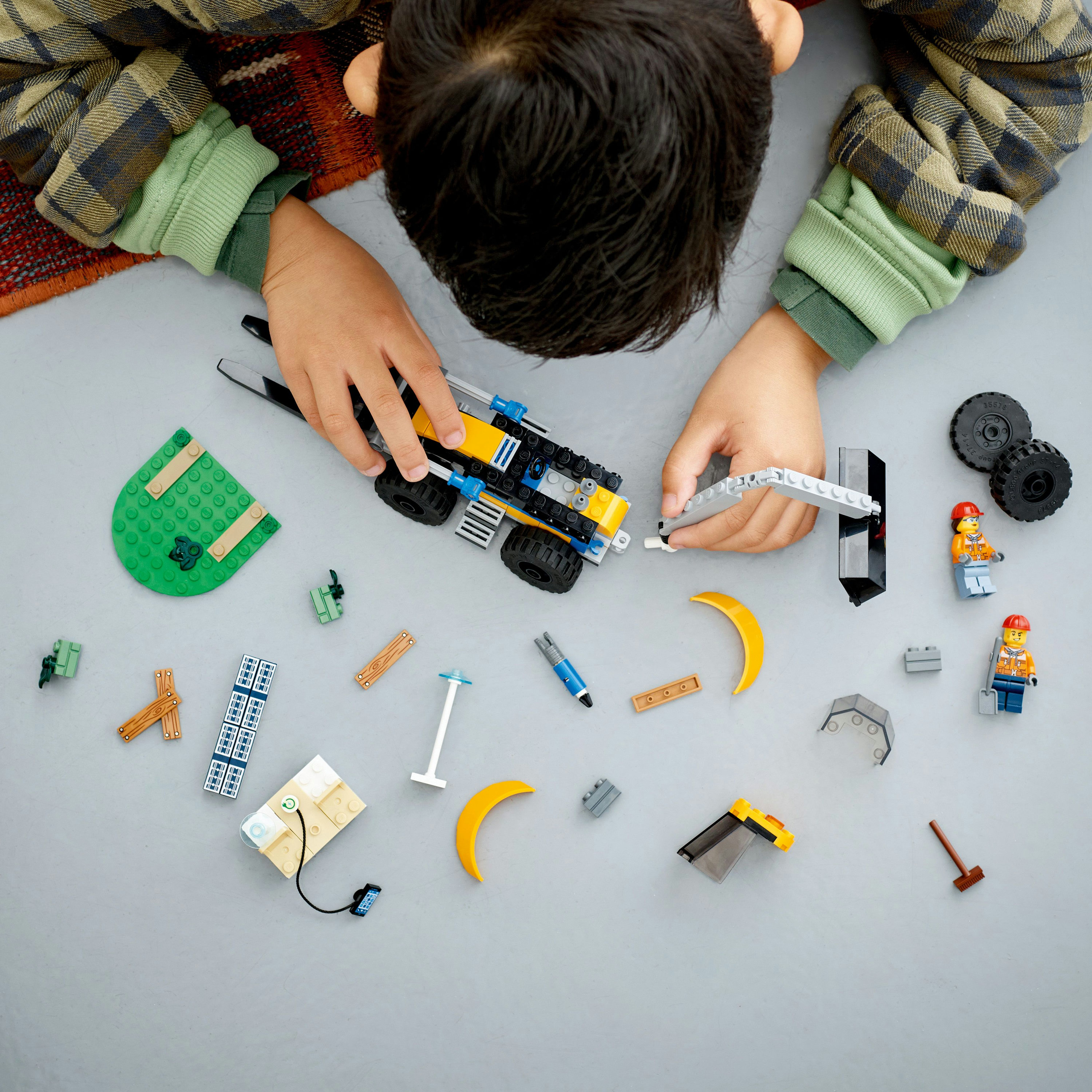 Ein Kind spielt mit Lego. Verschiedene Lego-Teile sind auf einer grauen Oberfläche verstreut. Sie bauen einen LKW.