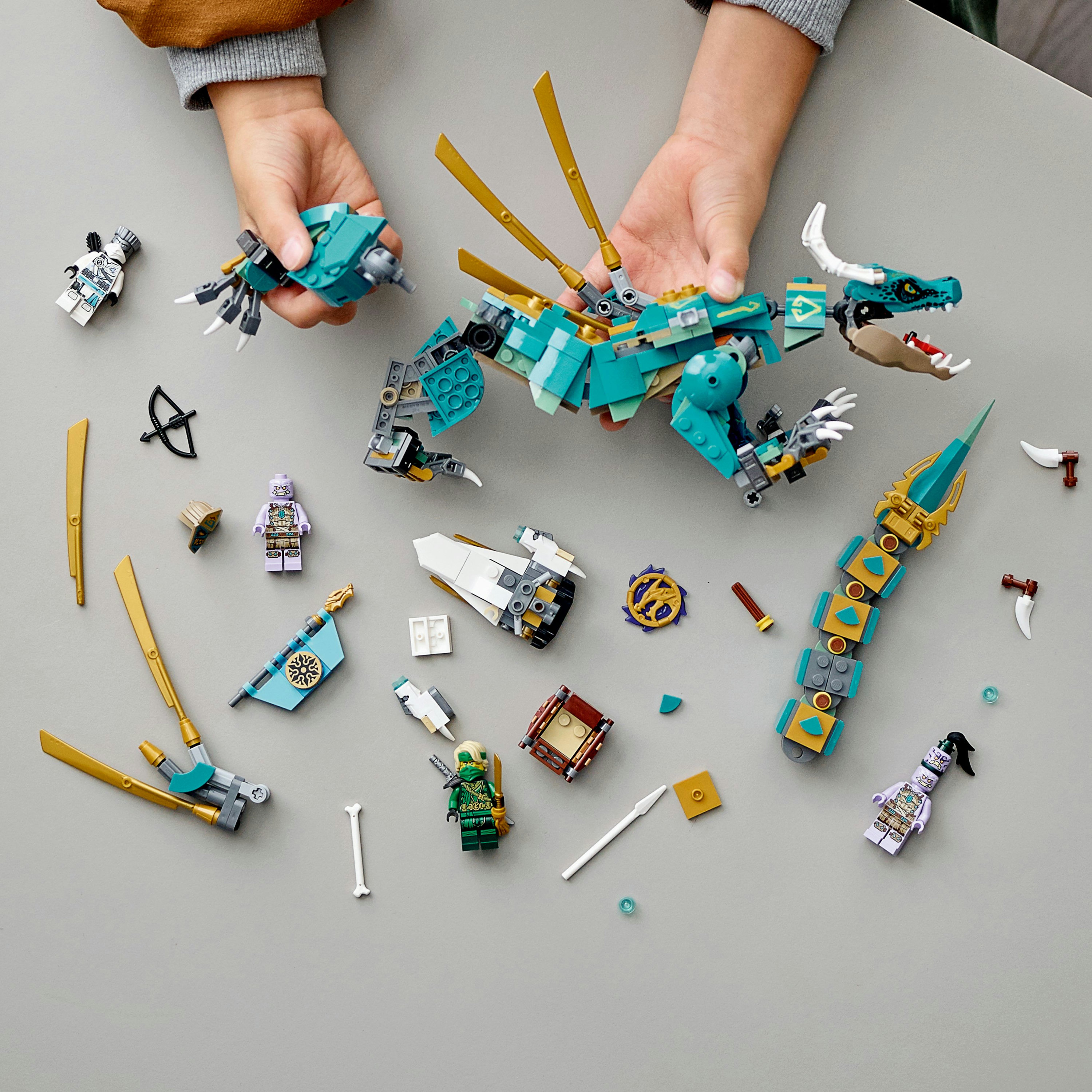 Eller Lego Ninjago ejderhası ve diğer Lego öğelerini tutuyor, gri bir arka planla.