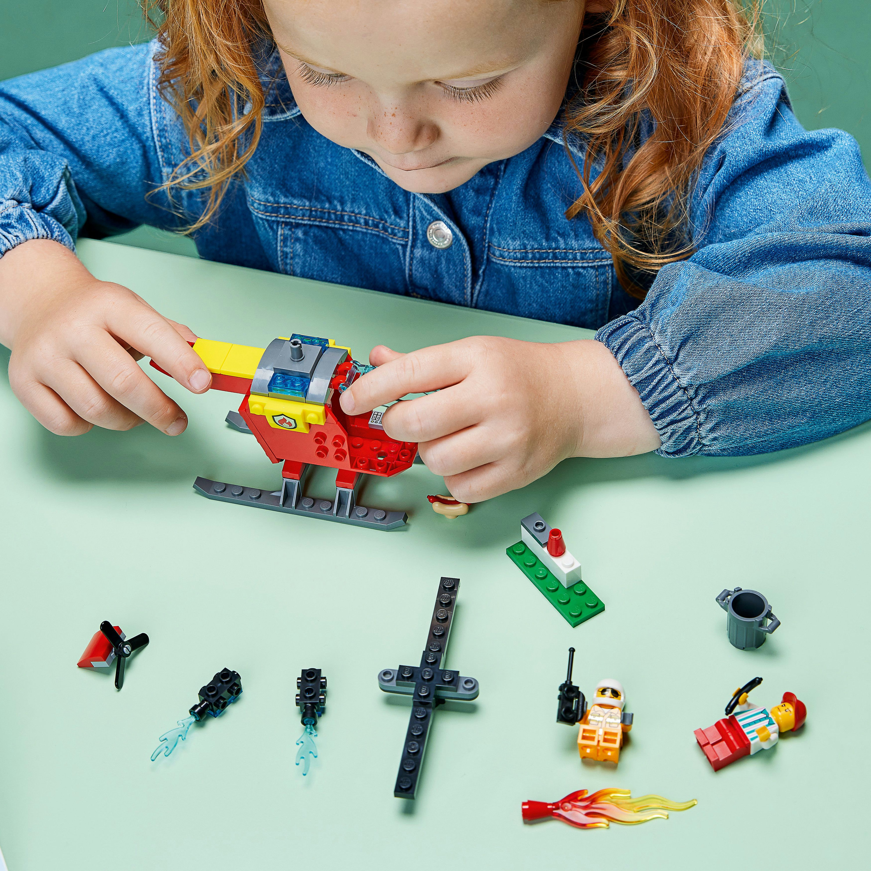 Kind spielt mit Lego. Roter und gelber Hubschrauber. Mehrere Lego-Teile liegen herum.