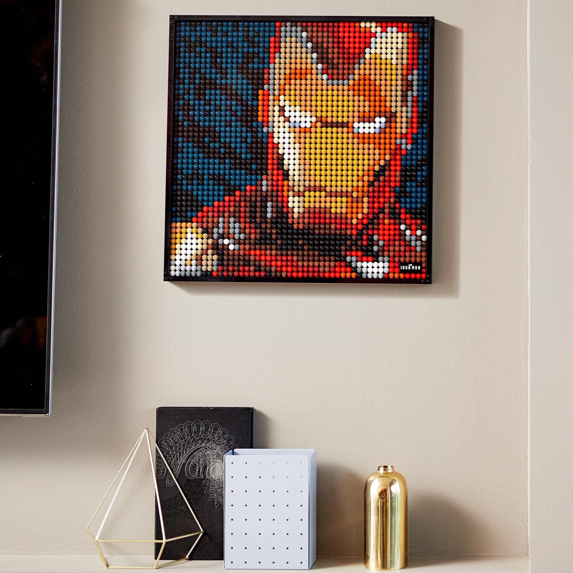 Iron Man portrait made of Lego bricks, in a black frame, displayed on a shelf with decor.