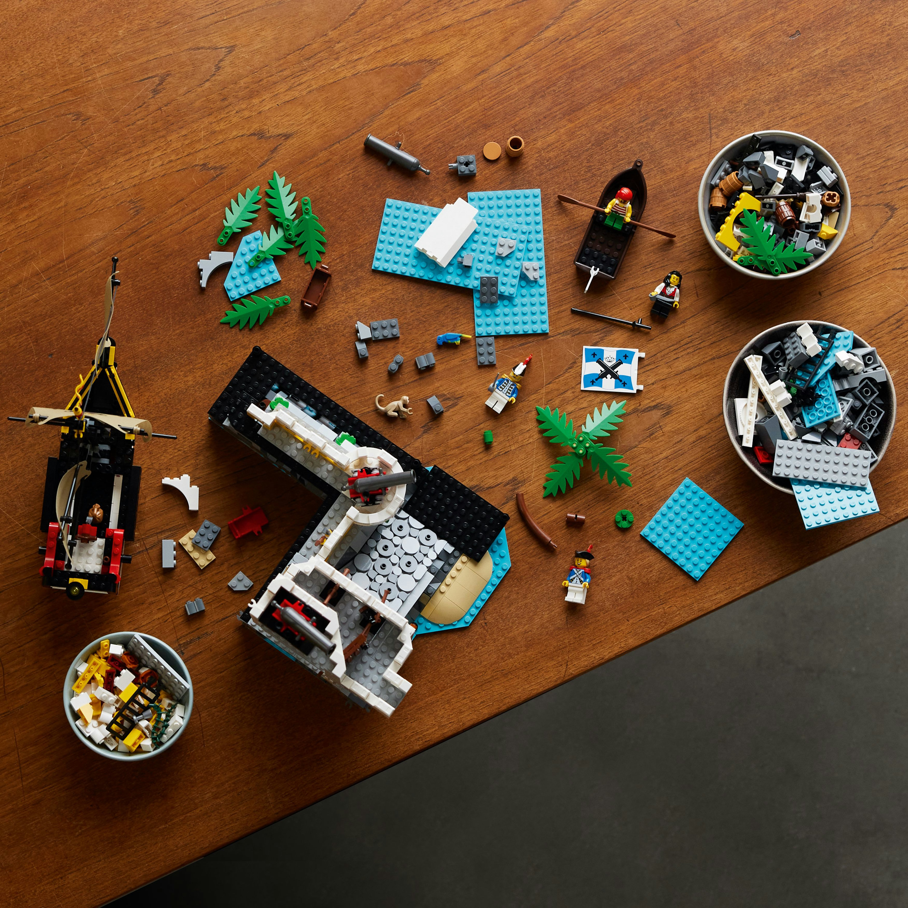 Zestaw Lego z elementami rozłożonymi na drewnianym stole. Zawiera łódź, figurki i elementy konstrukcyjne.
