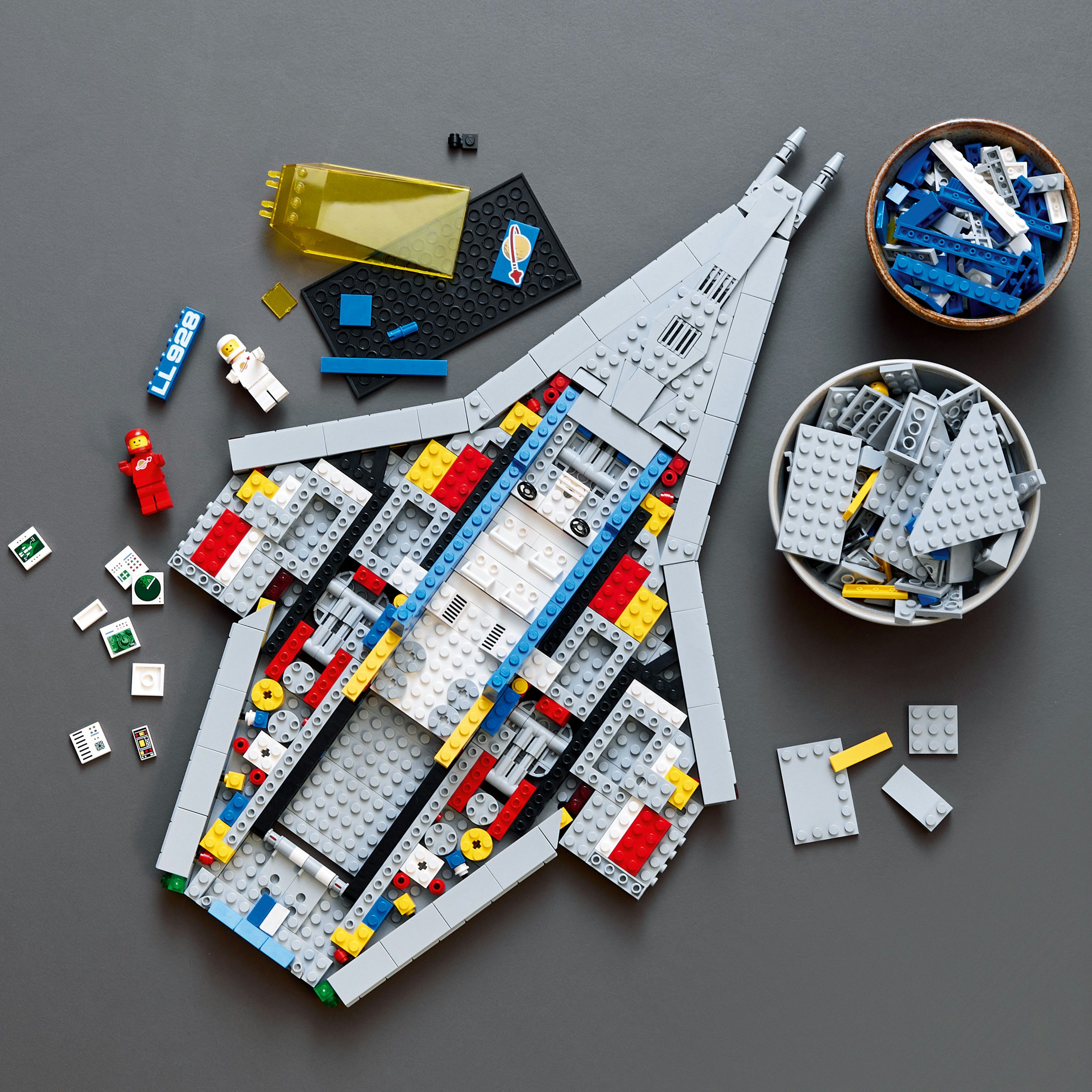 Modello di astronave grigia con interni colorati. Parti e minifig sparsi. Sfondo grigio.