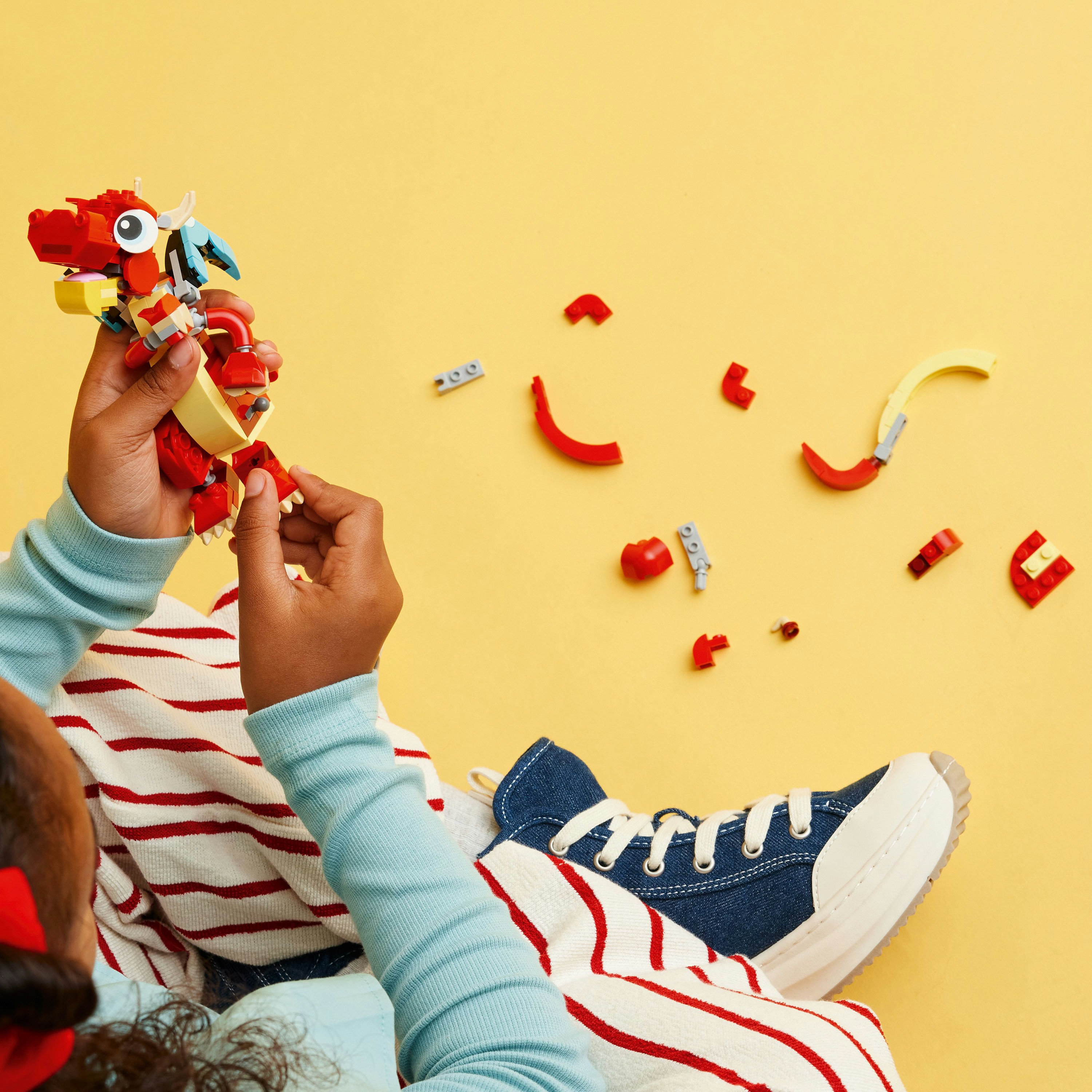 Un niño está construyendo un dragón LEGO rojo con piezas esparcidas sobre una superficie amarilla.