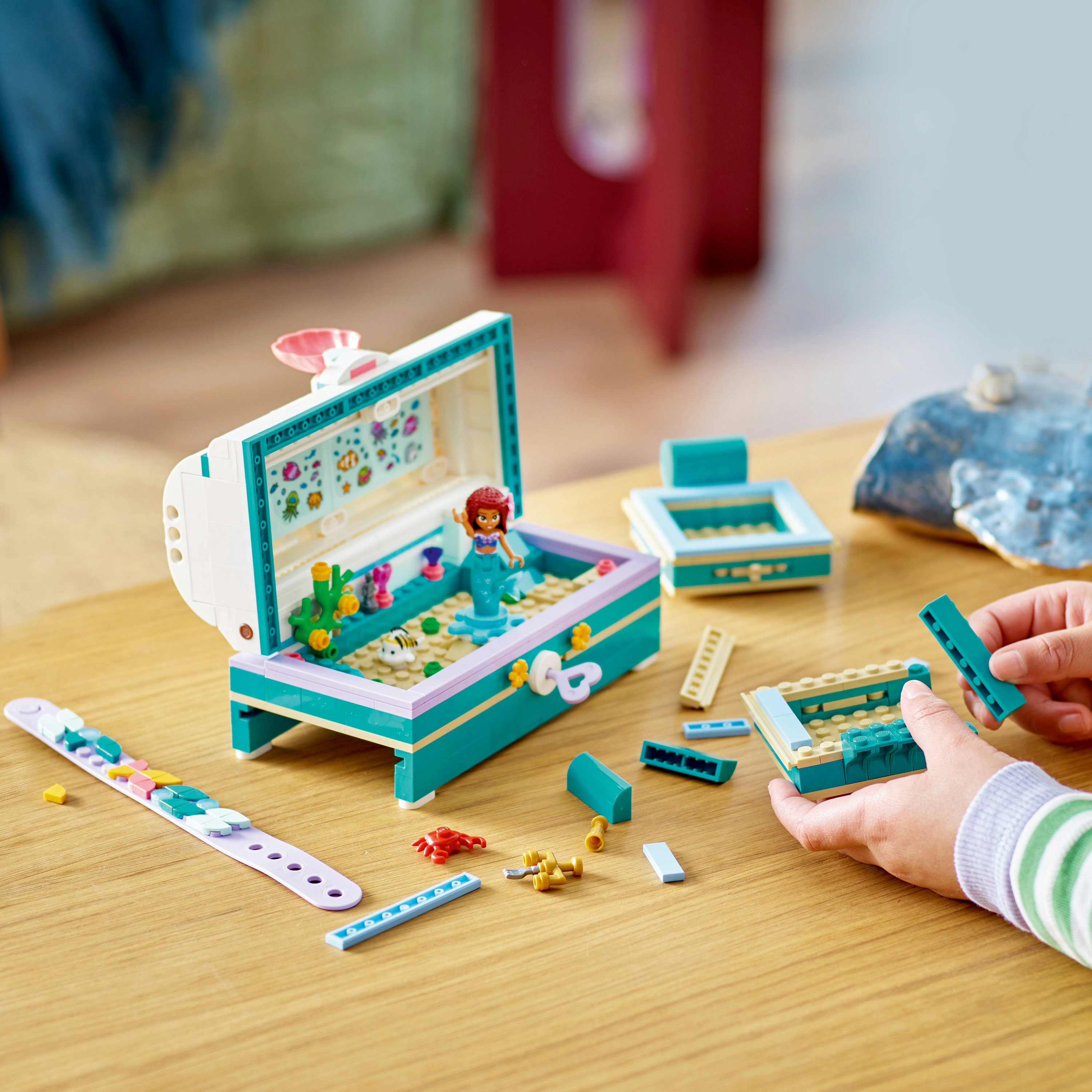 Zestaw Lego przedstawiający skrzynię skarbów z syreną. Części zestawu są rozrzucone na drewnianej powierzchni.