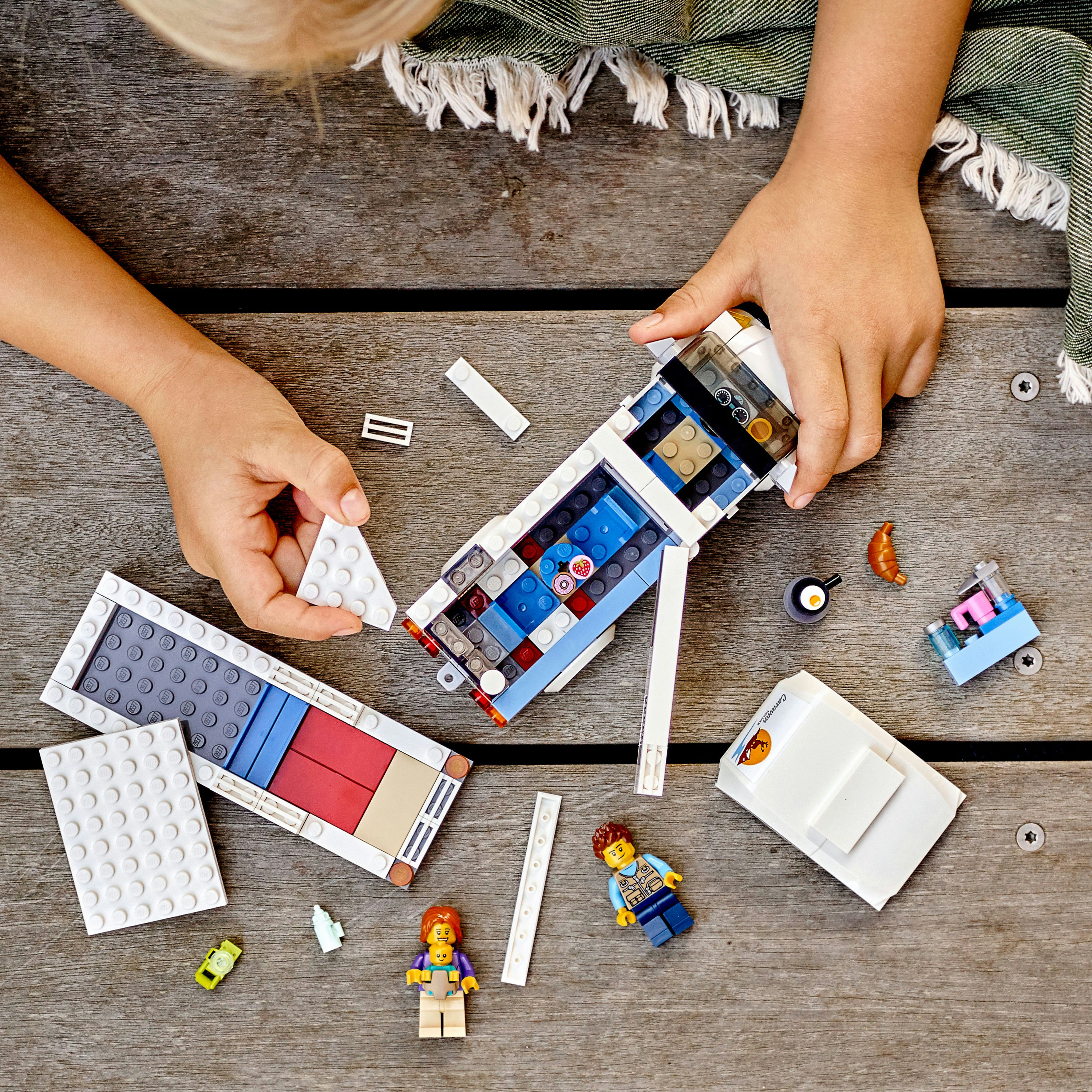 Een kind bouwt een Lego City set. Lego figuren en blokken liggen op een houten tafel.