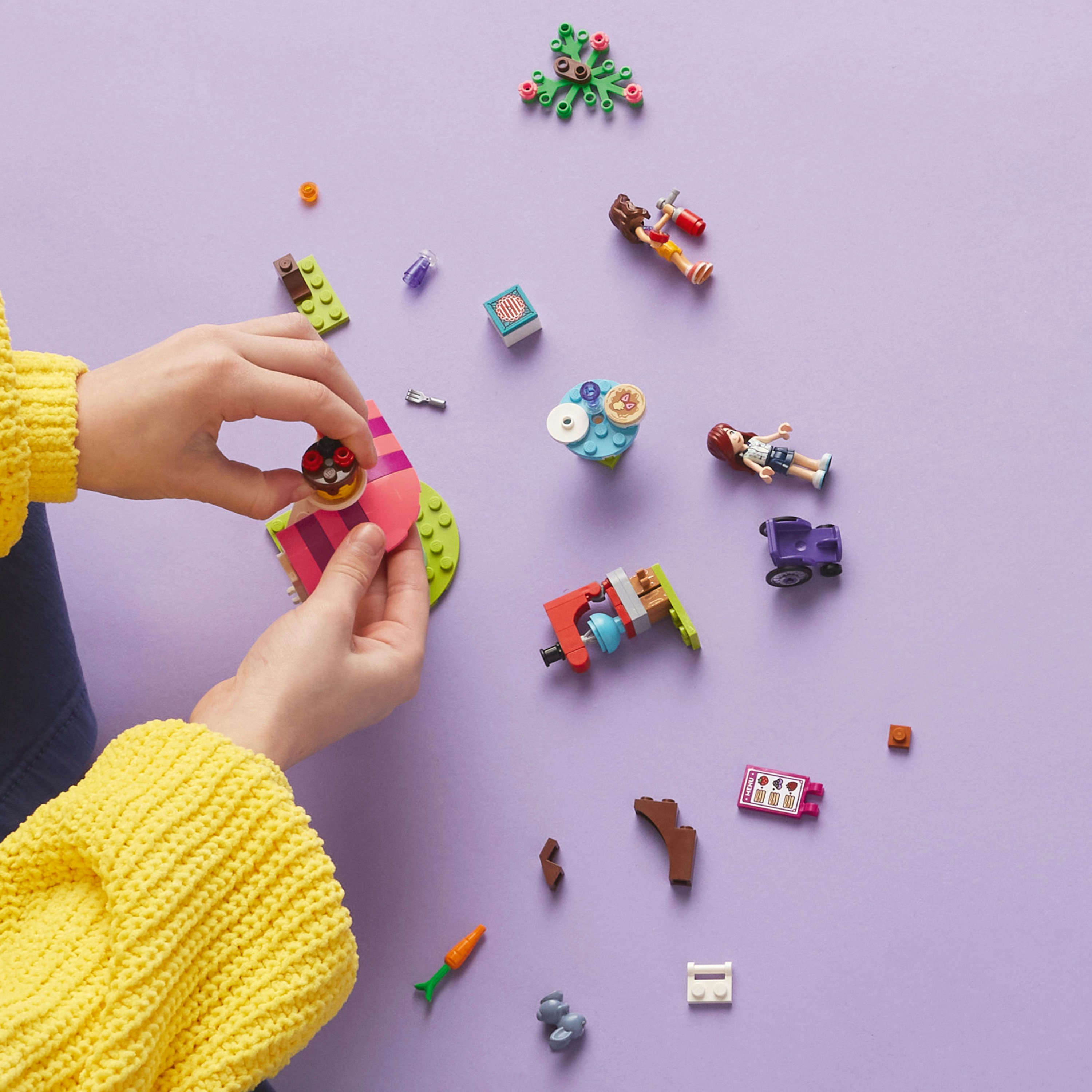 Çeşitli parçalara sahip bir Lego seti ve bir çocuğun elleri onları mor bir yüzeye birleştiriyor.