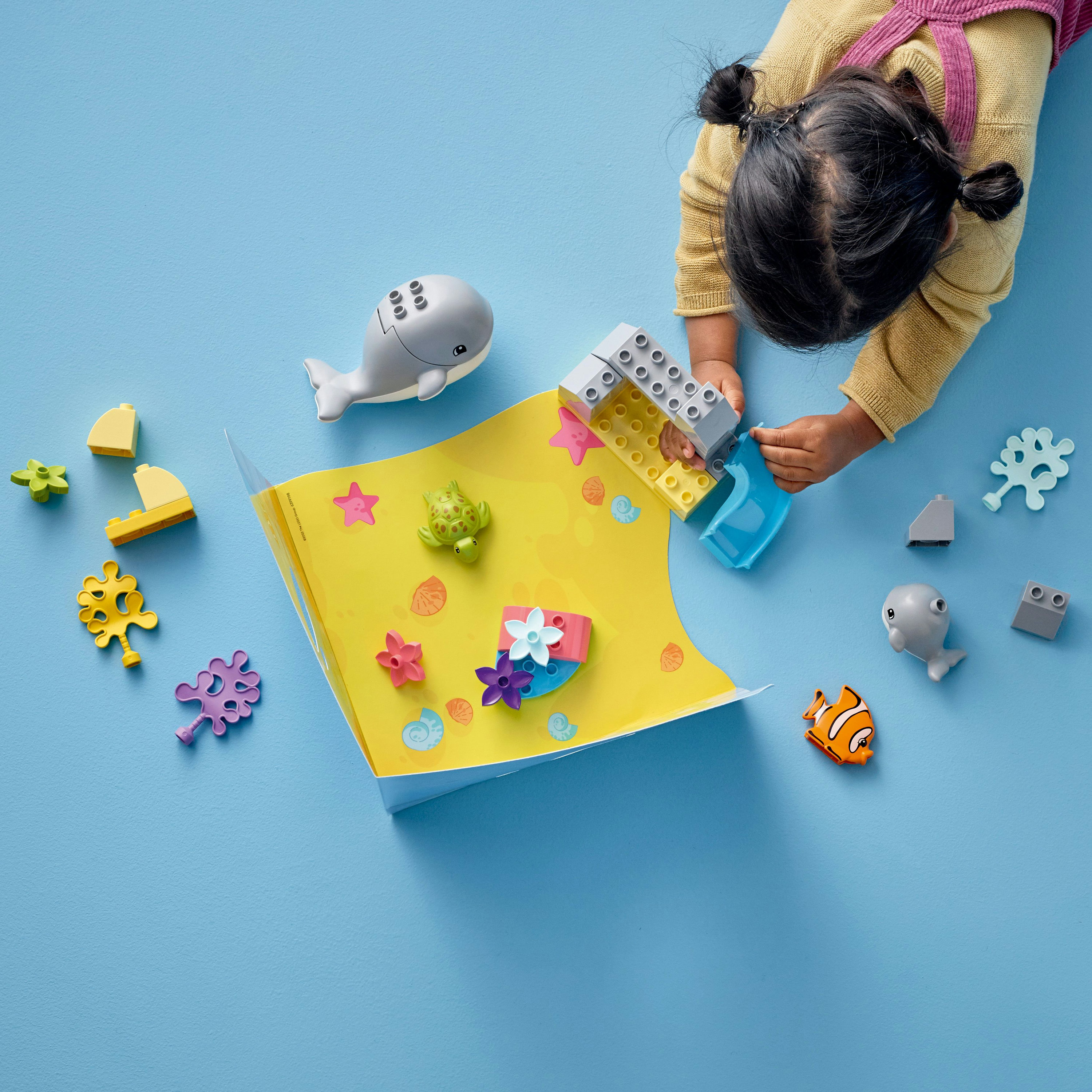 Ein Kind spielt mit Duplo-Steinen und arrangiert verschiedene Figuren und Strukturen zum Thema Meer.
