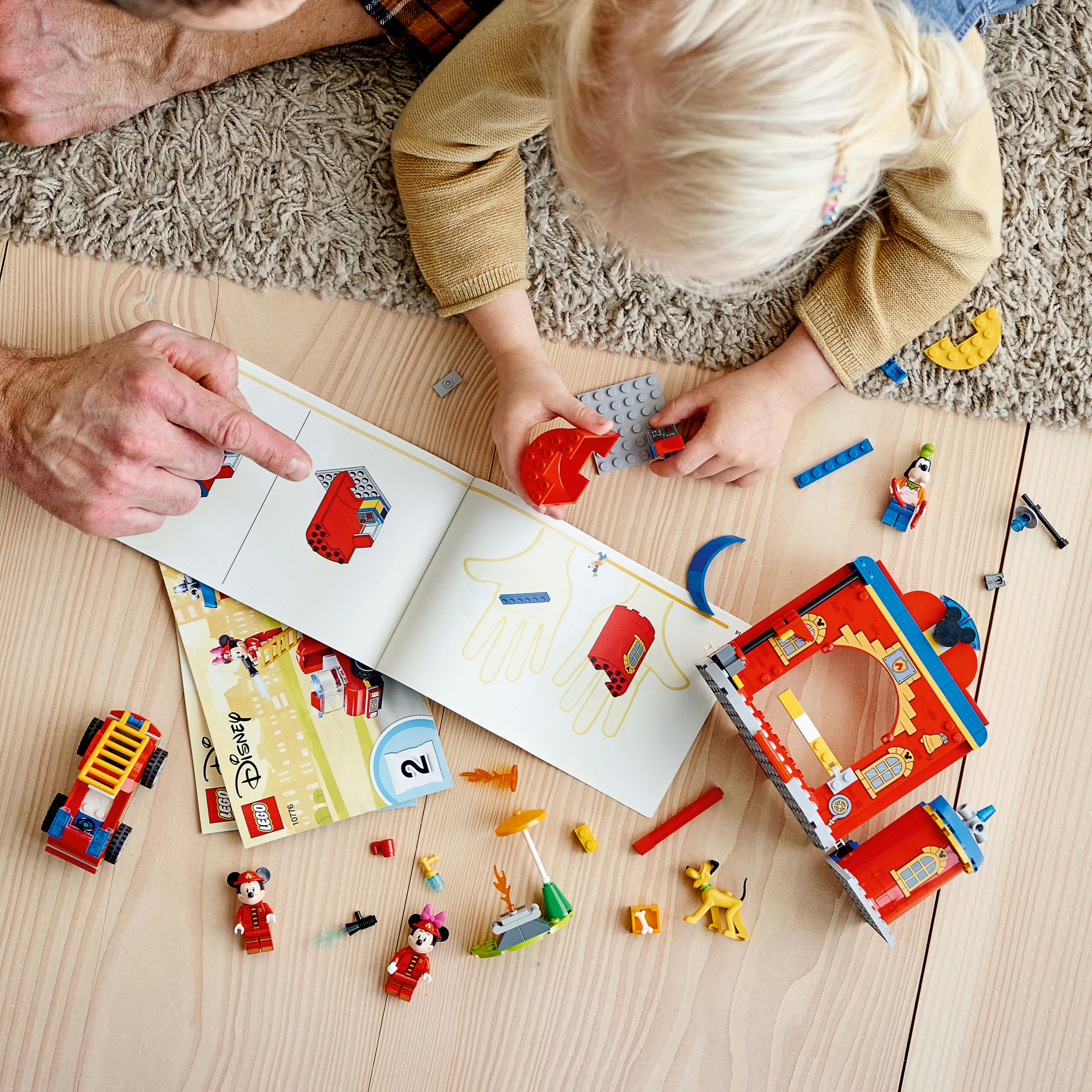 Kind und Erwachsener bauen Lego-Set. Offene Anweisungen und Lego-Teile auf Holzboden.