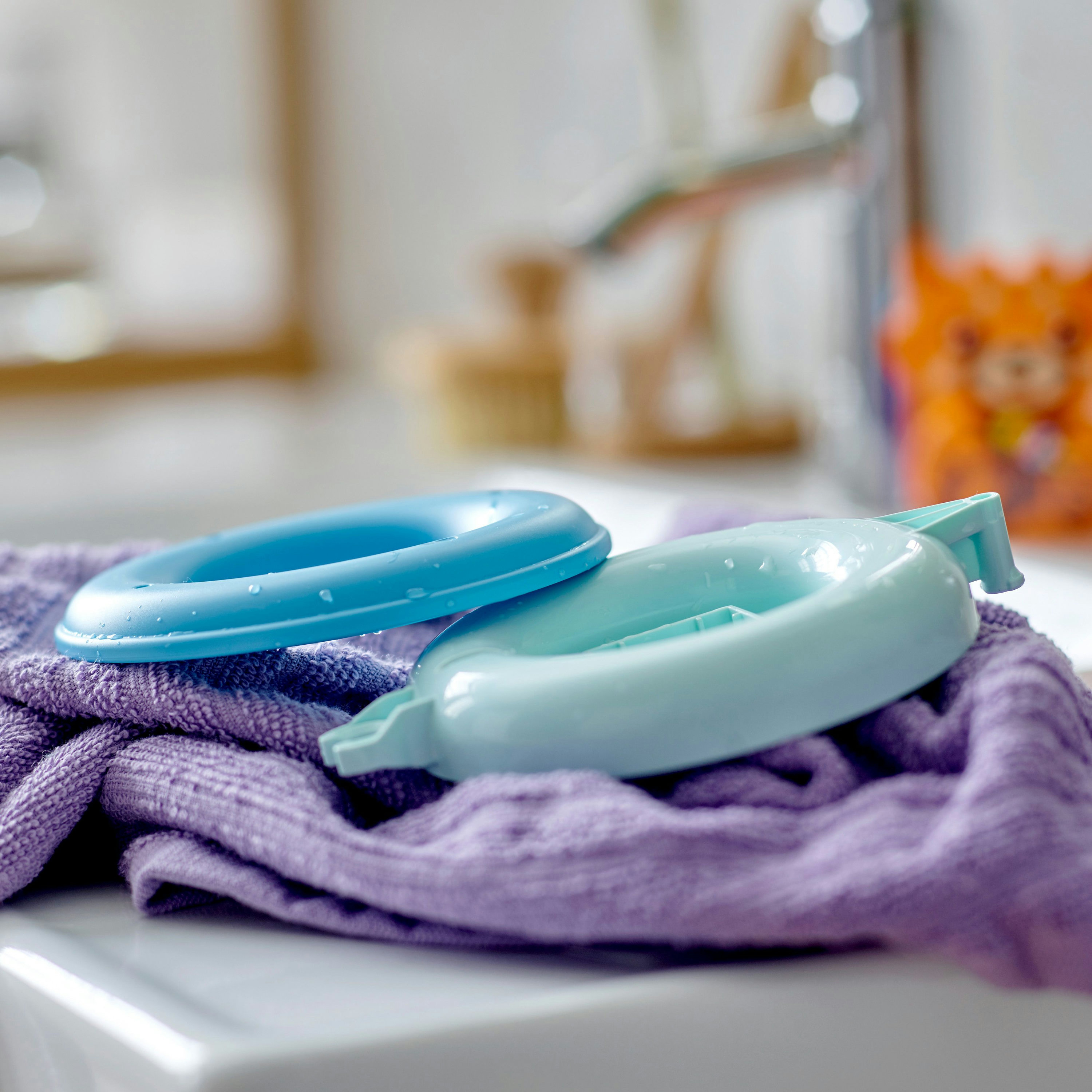 Due anelli Lego blu e azzurri su un asciugamano viola, con uno sfondo sfocato di un'area lavabo.
