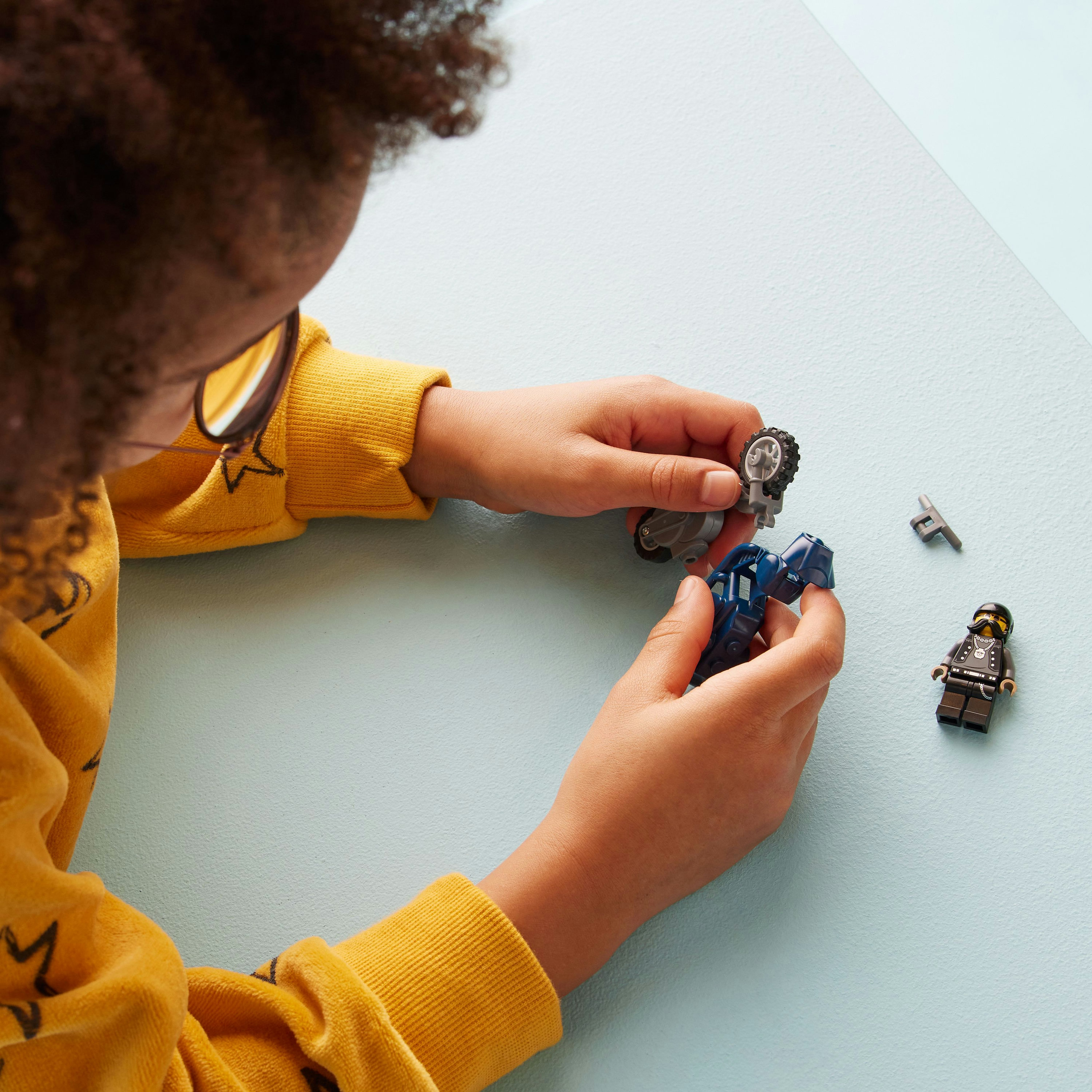 Ein Kind baut ein Lego-Motorrad zusammen. Teile sind auf hellblauem Untergrund verstreut.