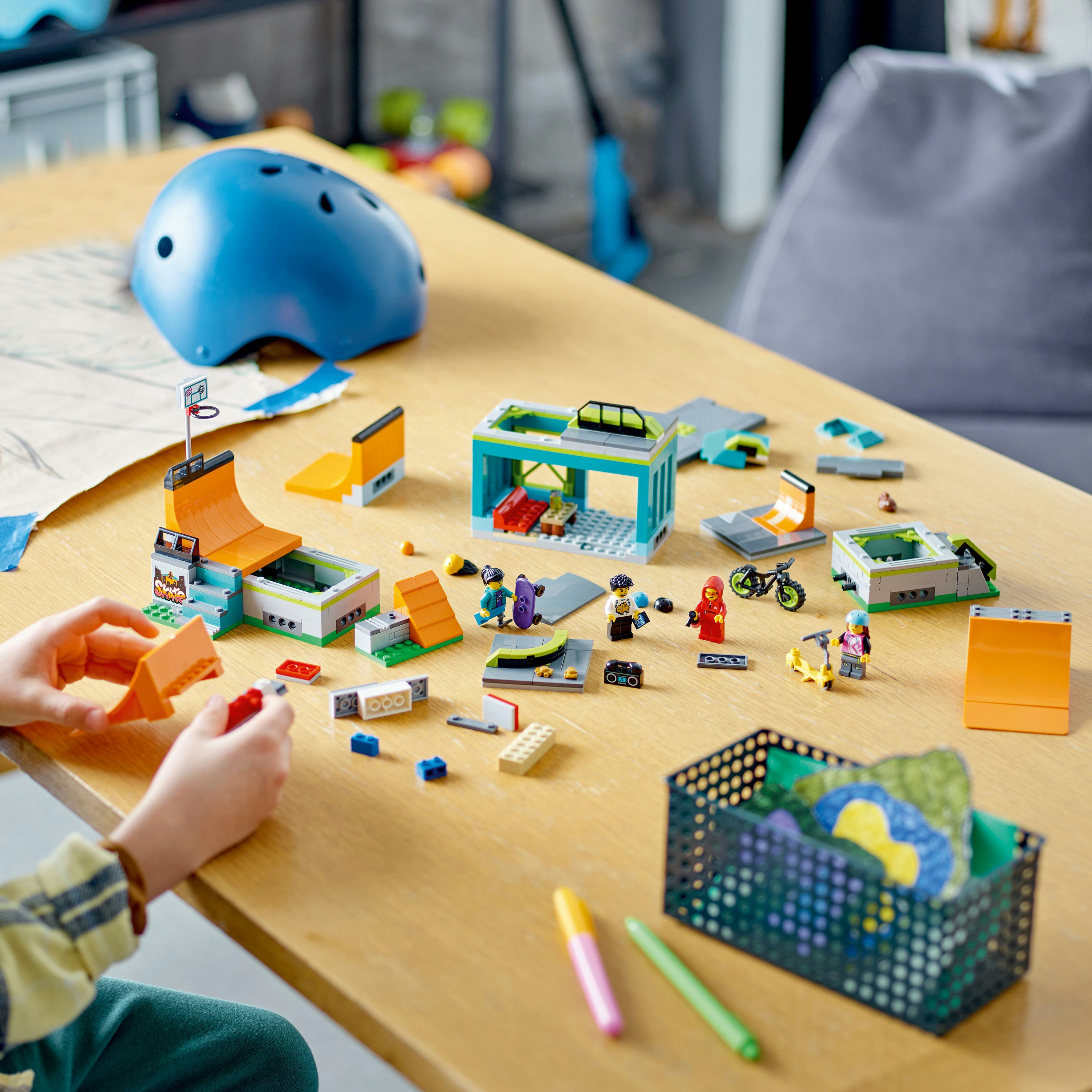 Lego-Set mit Skatepark-Elementen, Figuren und einem blauen Helm auf einem Holztisch.