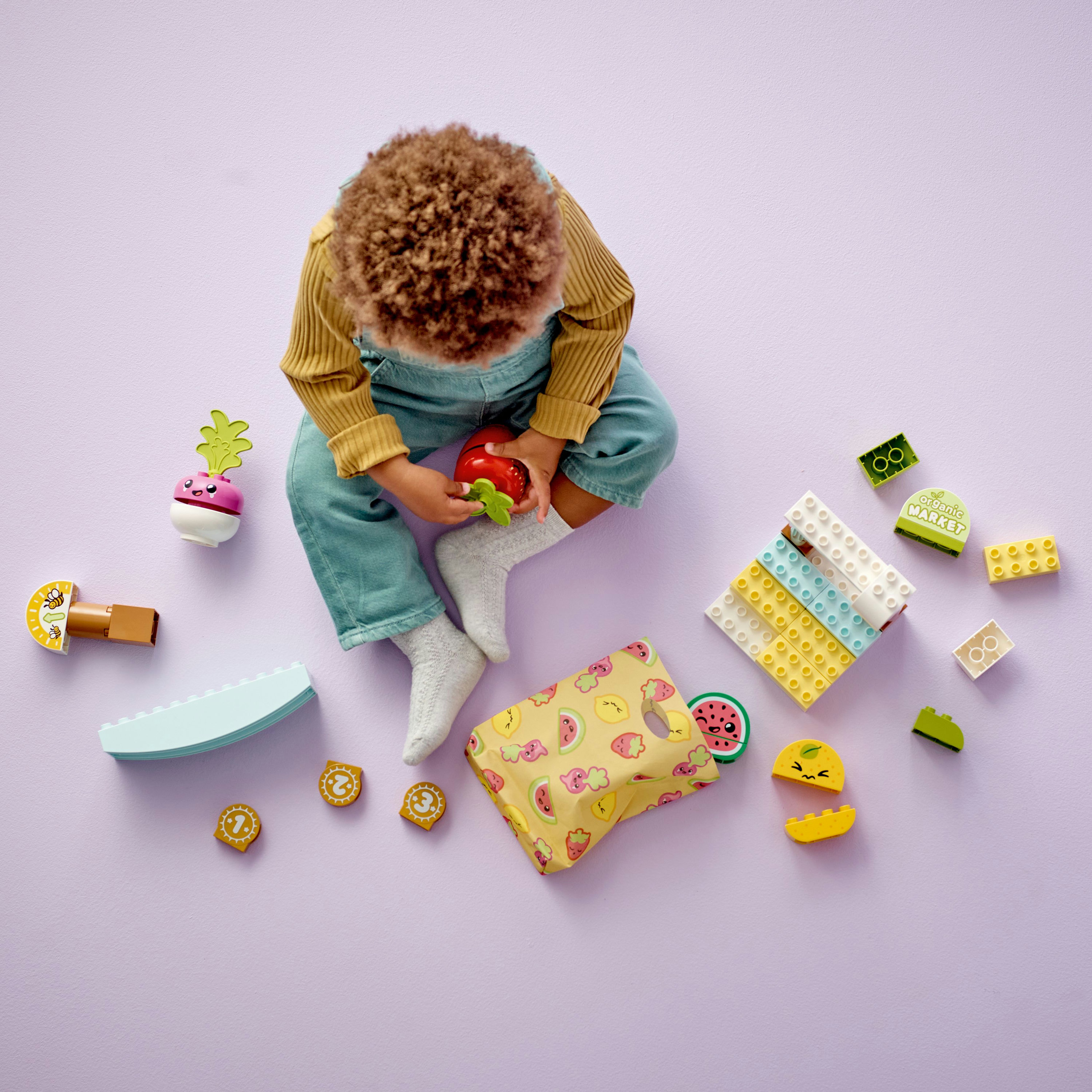 Ein Kind spielt mit Lego Duplo Obst und Gemüse auf einer lila Oberfläche.