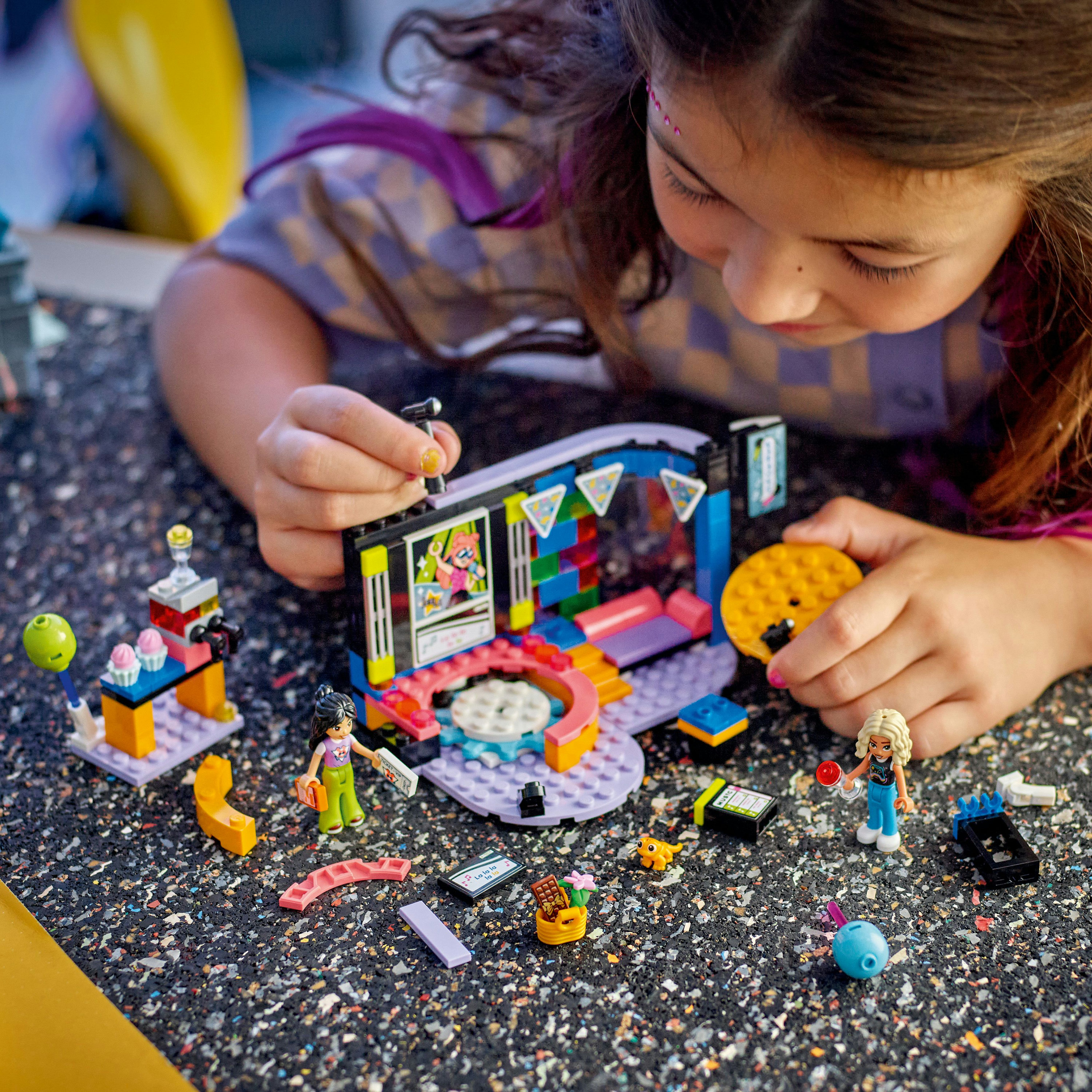 Meisje speelt met LEGO Friends set, met een podium, minifiguren en diverse kleurrijke accessoires.