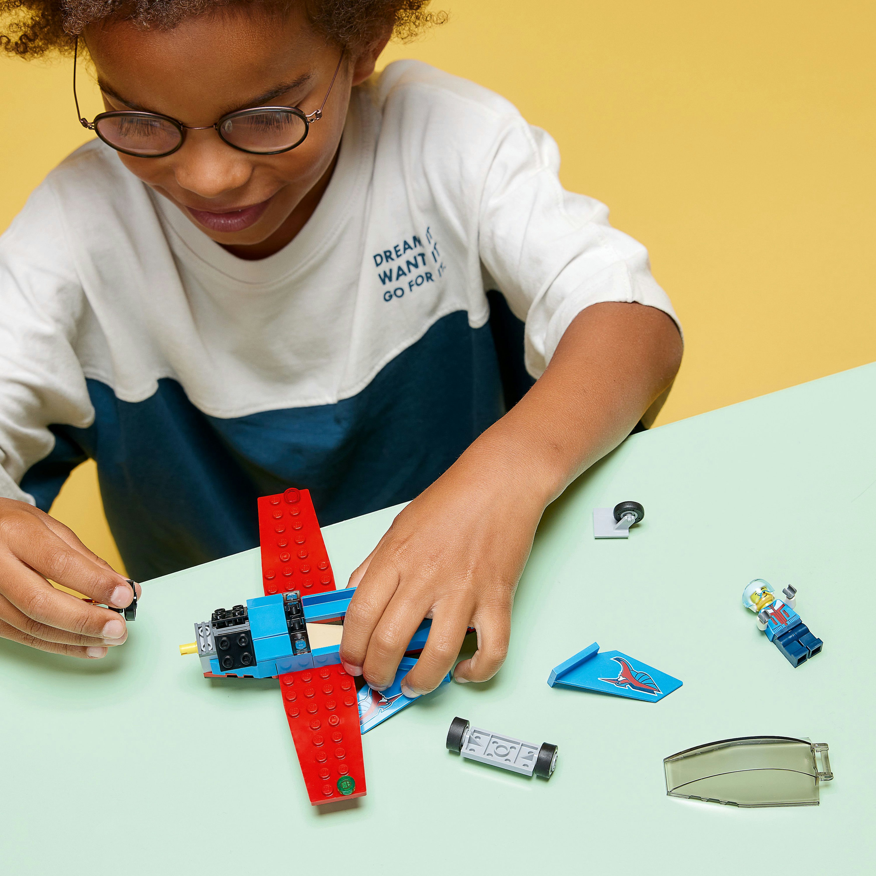 Ein Kind baut ein rotes und blaues Lego-Flugzeug, mit anderen Legoteilen in der Nähe.