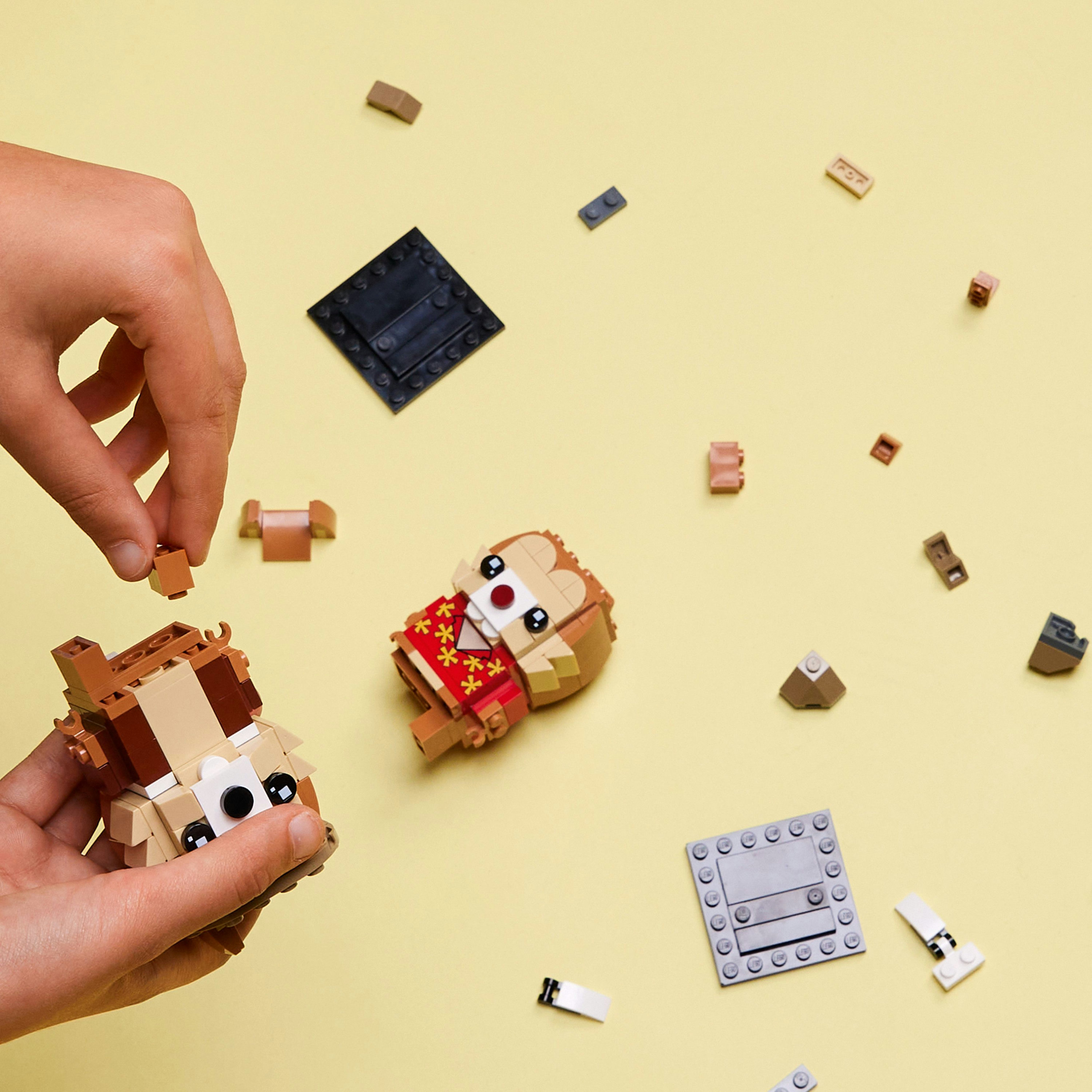 Hände, die eine Lego-Affenfigur auf gelber Oberfläche zusammensetzen. Verstreute Lego-Steine darum herum.