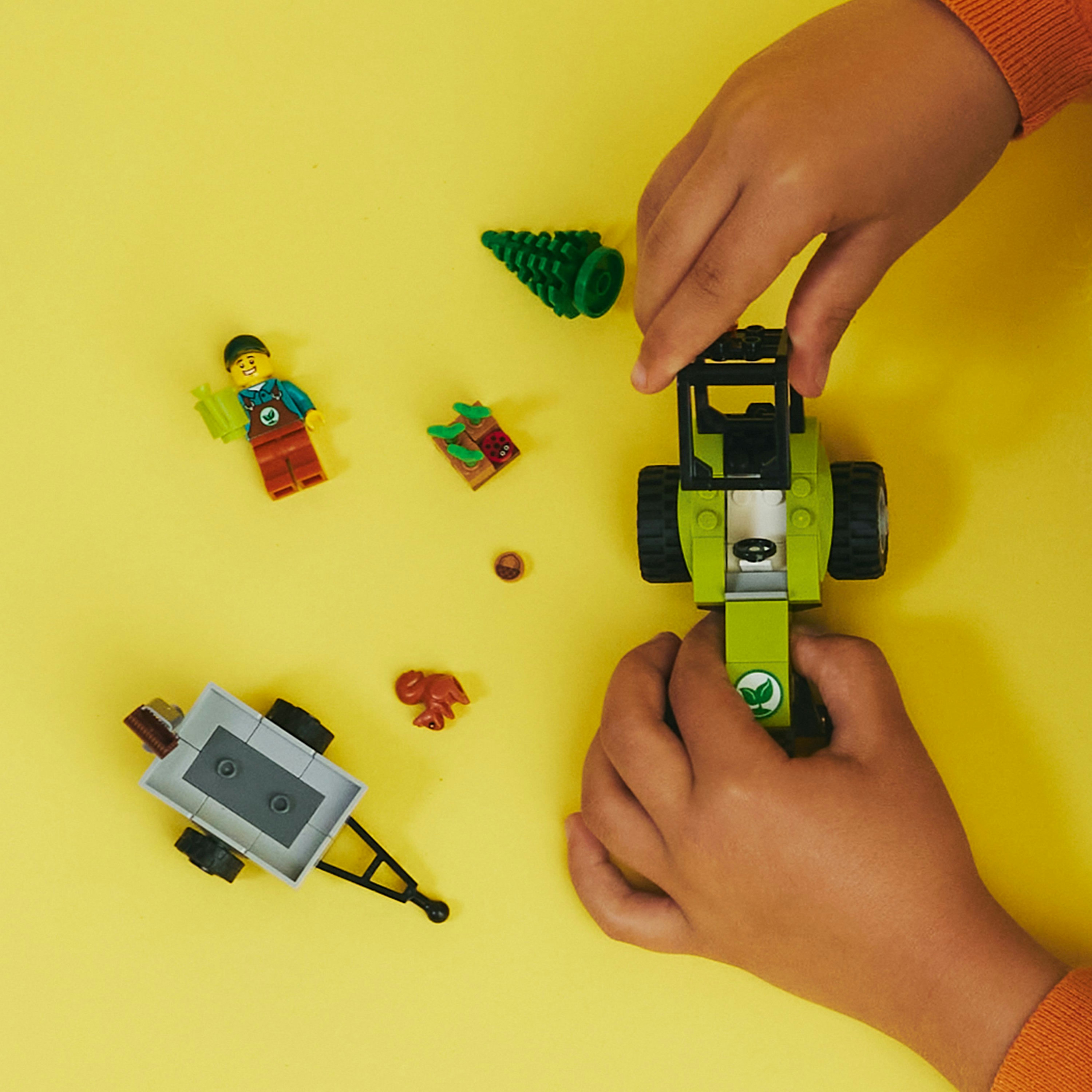 Kinderhände interagieren mit einem grünen Traktor und einem LEGO-Set zum Thema Bauernhof auf Gelb.