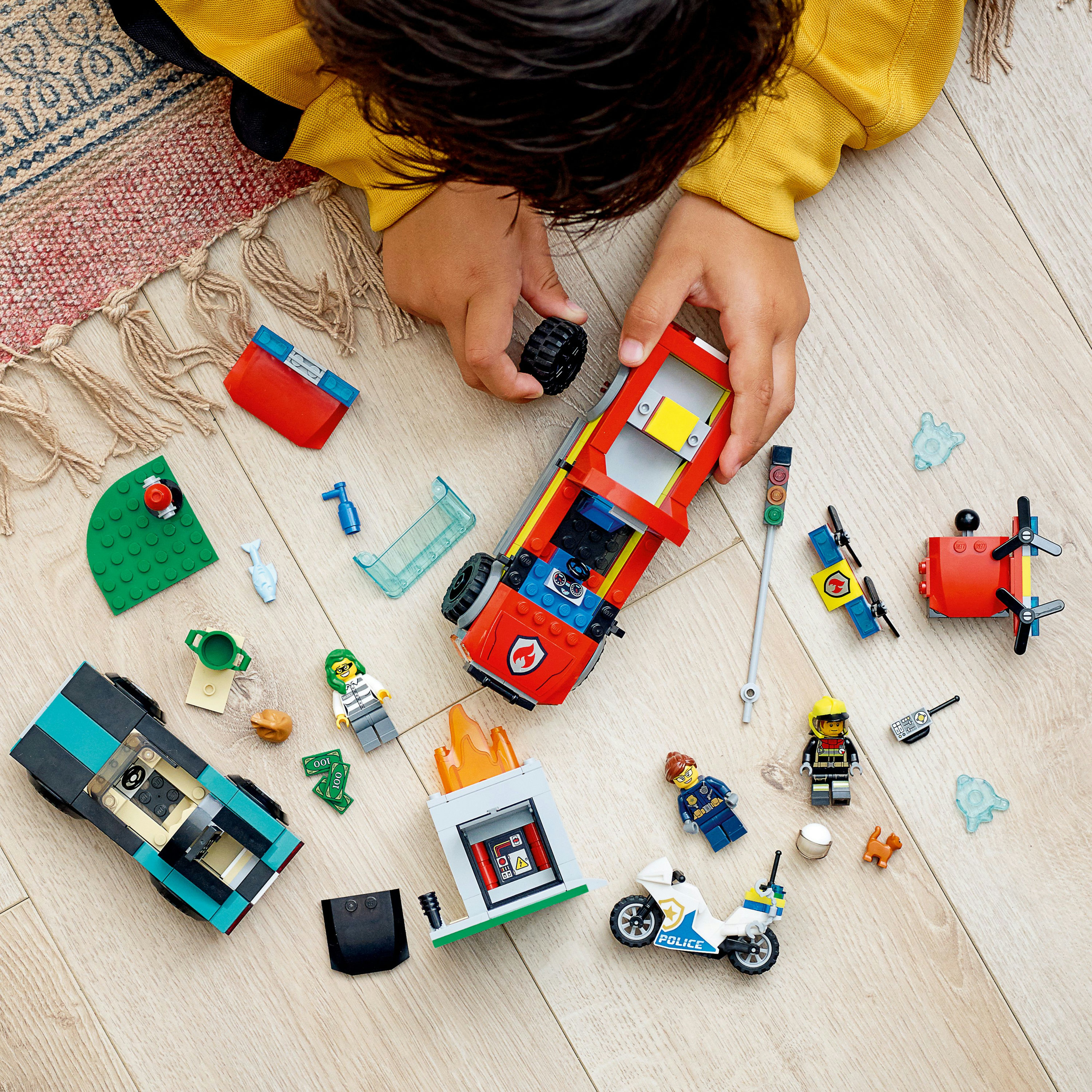 Niño jugando con un set de Lego City. Incluye un coche rojo, un edificio en llamas y figuras Lego.